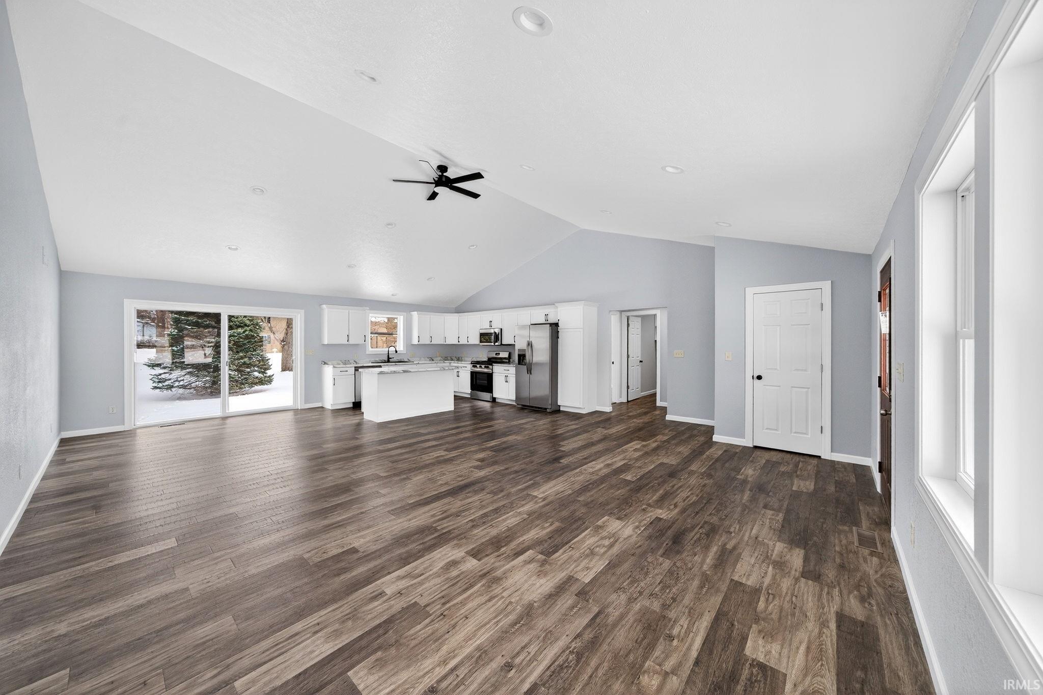 Unfurnished living room featuring ceiling fan, dark wood-style floors, and a high ceiling