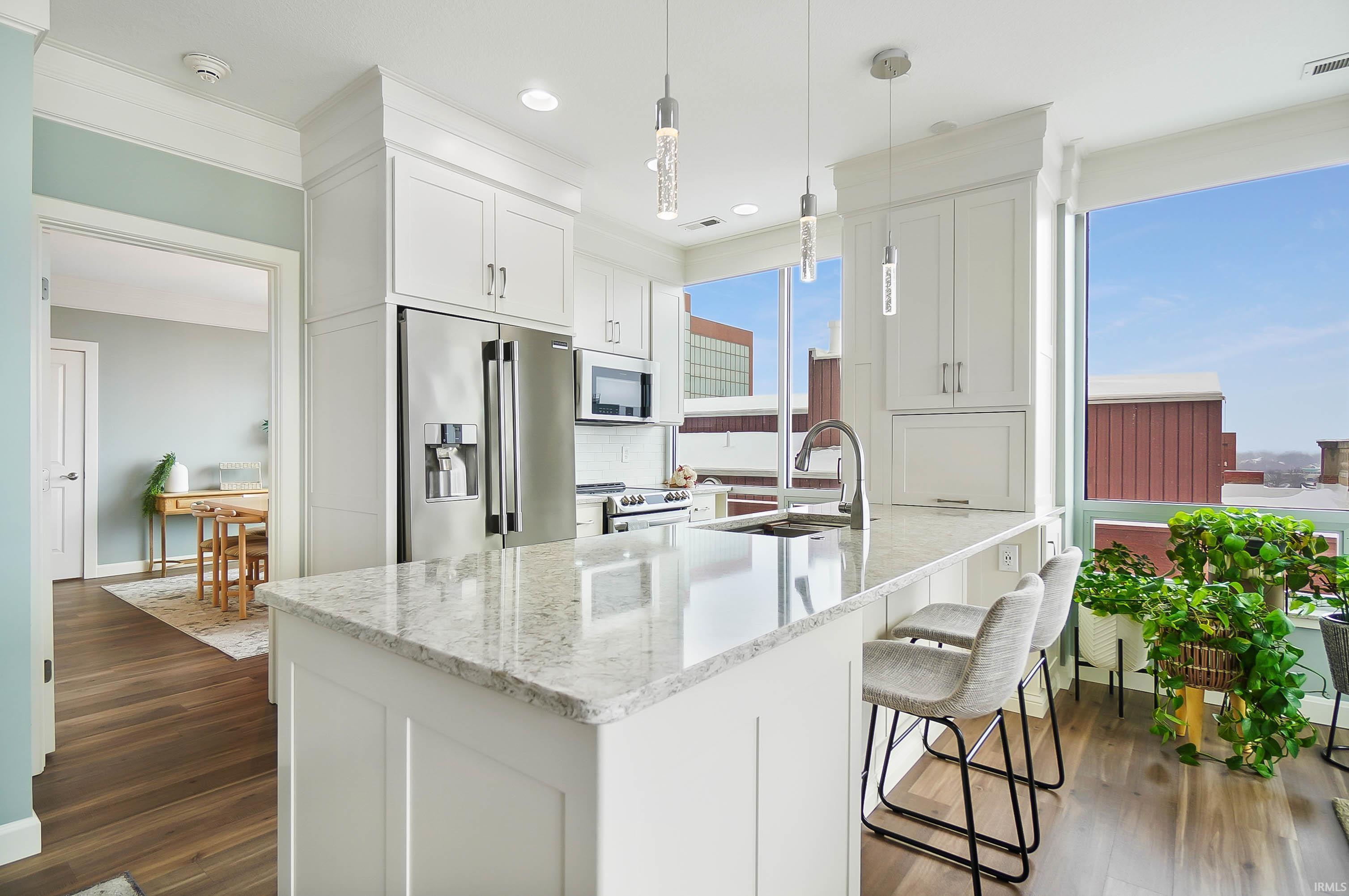 Kitchen featuring light stone counters, stainless steel appliances, white cabinets, dark wood-type flooring, and a peninsula