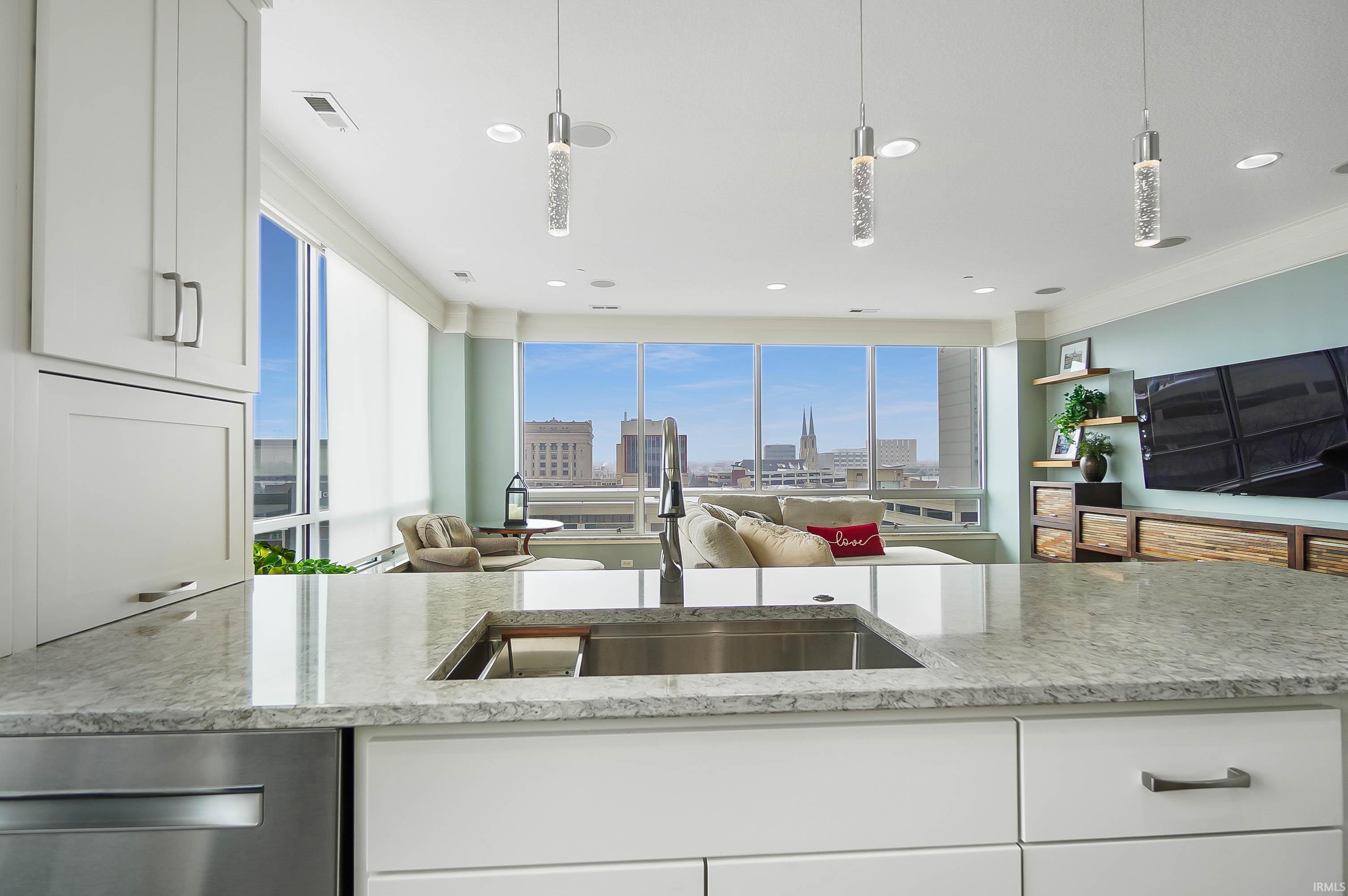 Kitchen with white cabinets, light stone counters, open floor plan, and pendant lighting
