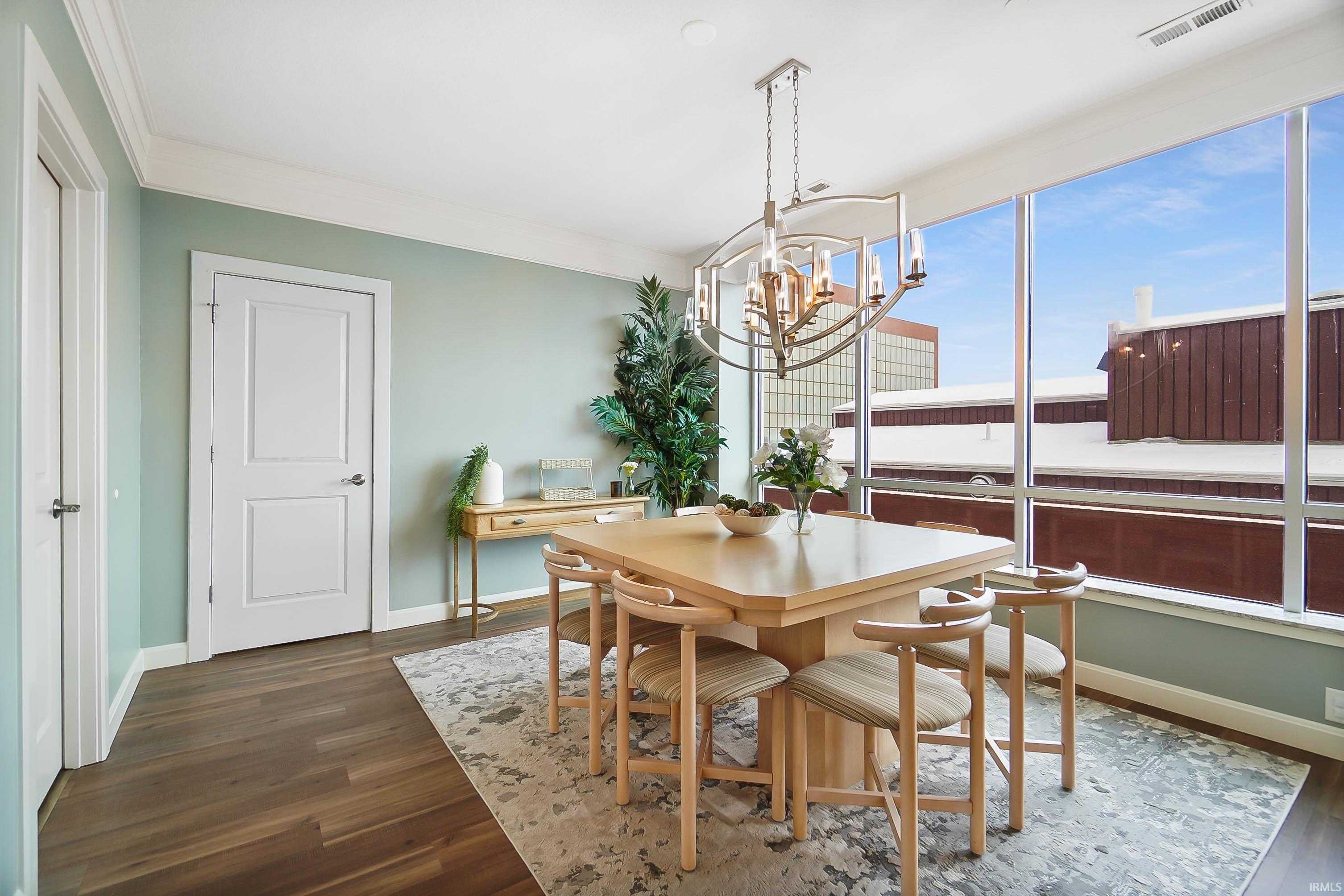 Dining area with dark wood-style flooring, hanging lights, and crown molding