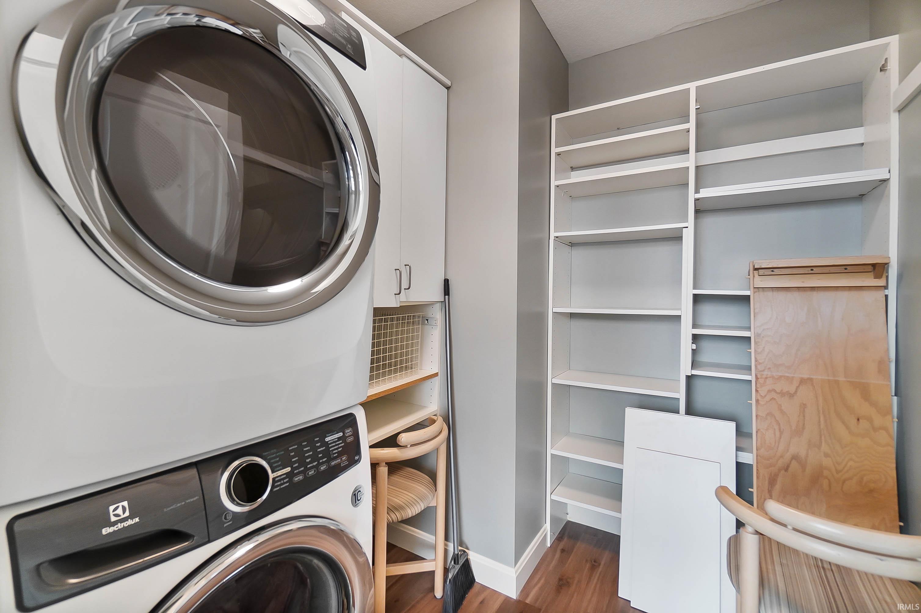 Laundry area with stacked washer and clothes dryer and dark wood-style floors