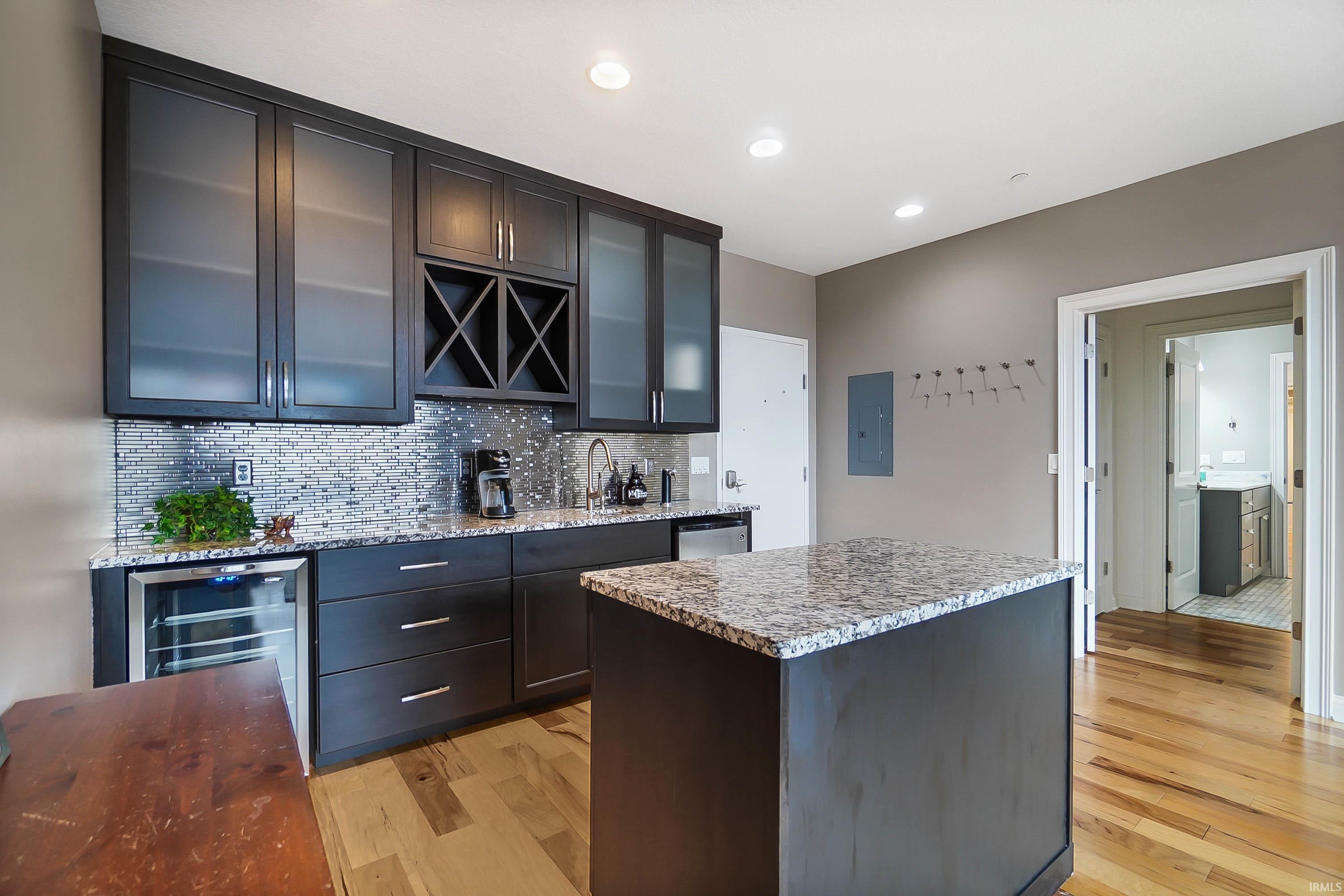 Kitchen with light stone counters, wine cooler, backsplash, a center island, and light wood-type flooring