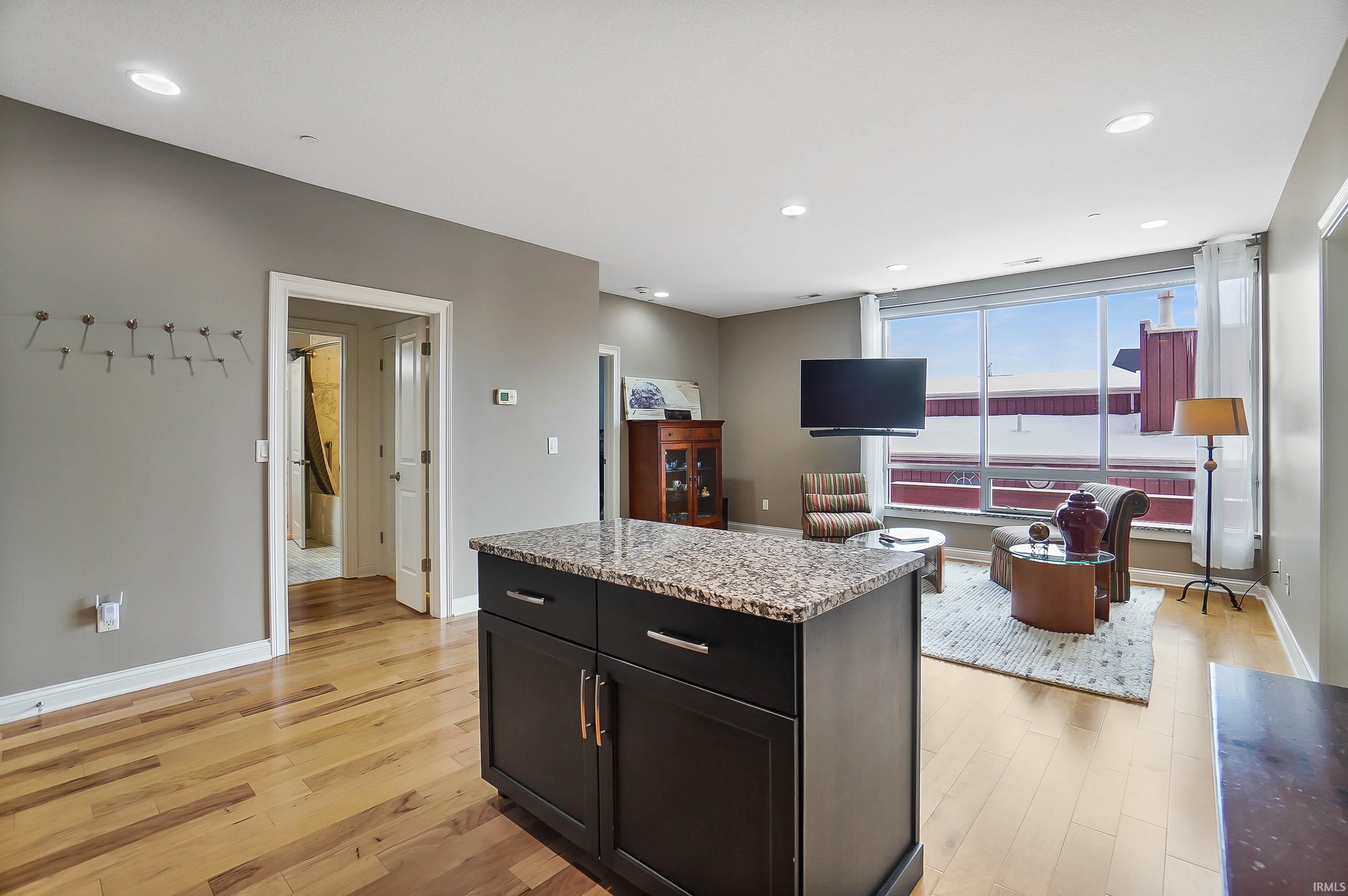 Kitchen with light stone counters, dark cabinetry, light wood-type flooring, a kitchen island, and recessed lighting