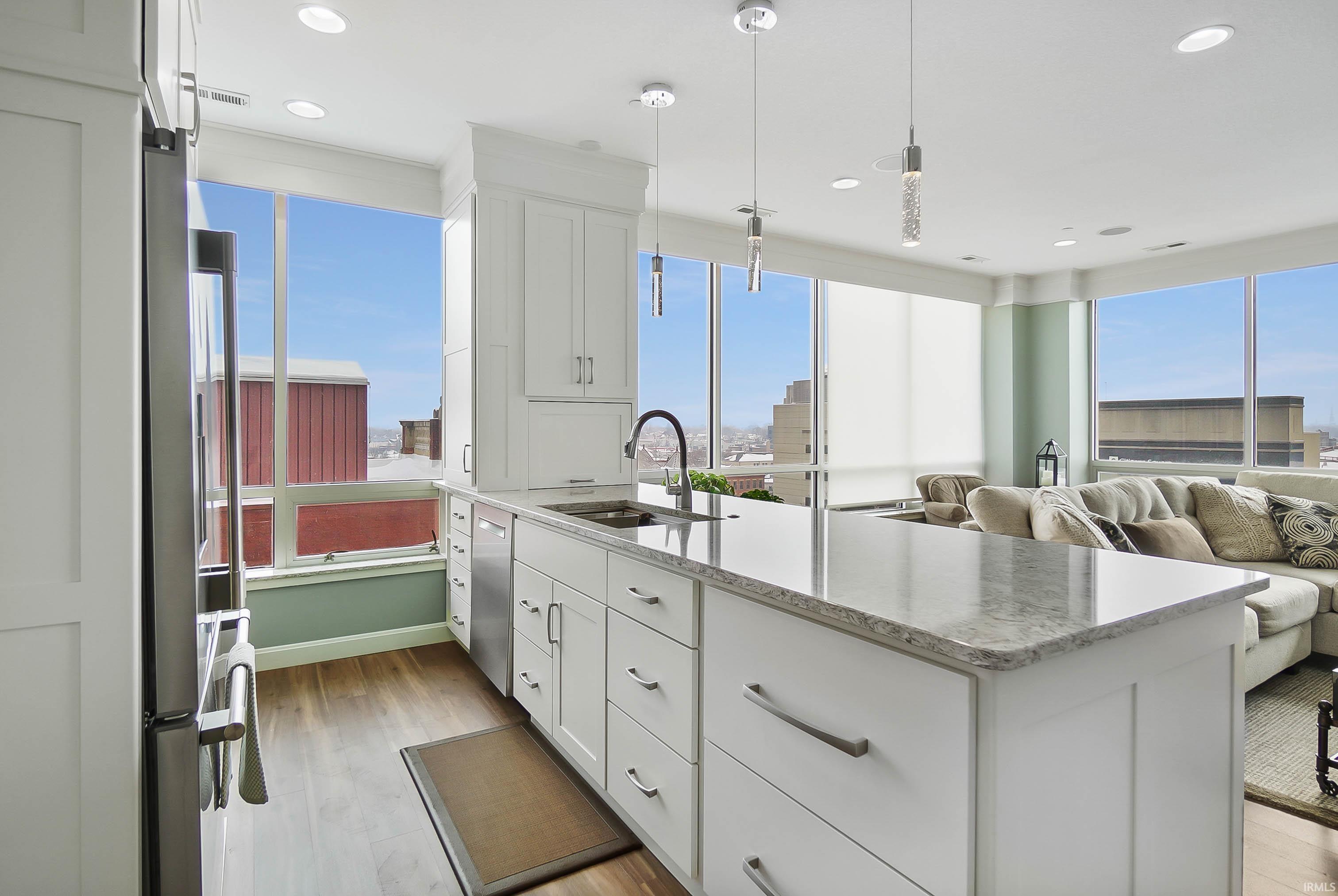 Kitchen with open floor plan, light stone countertops, white cabinets, stainless steel appliances, and light wood-style floors