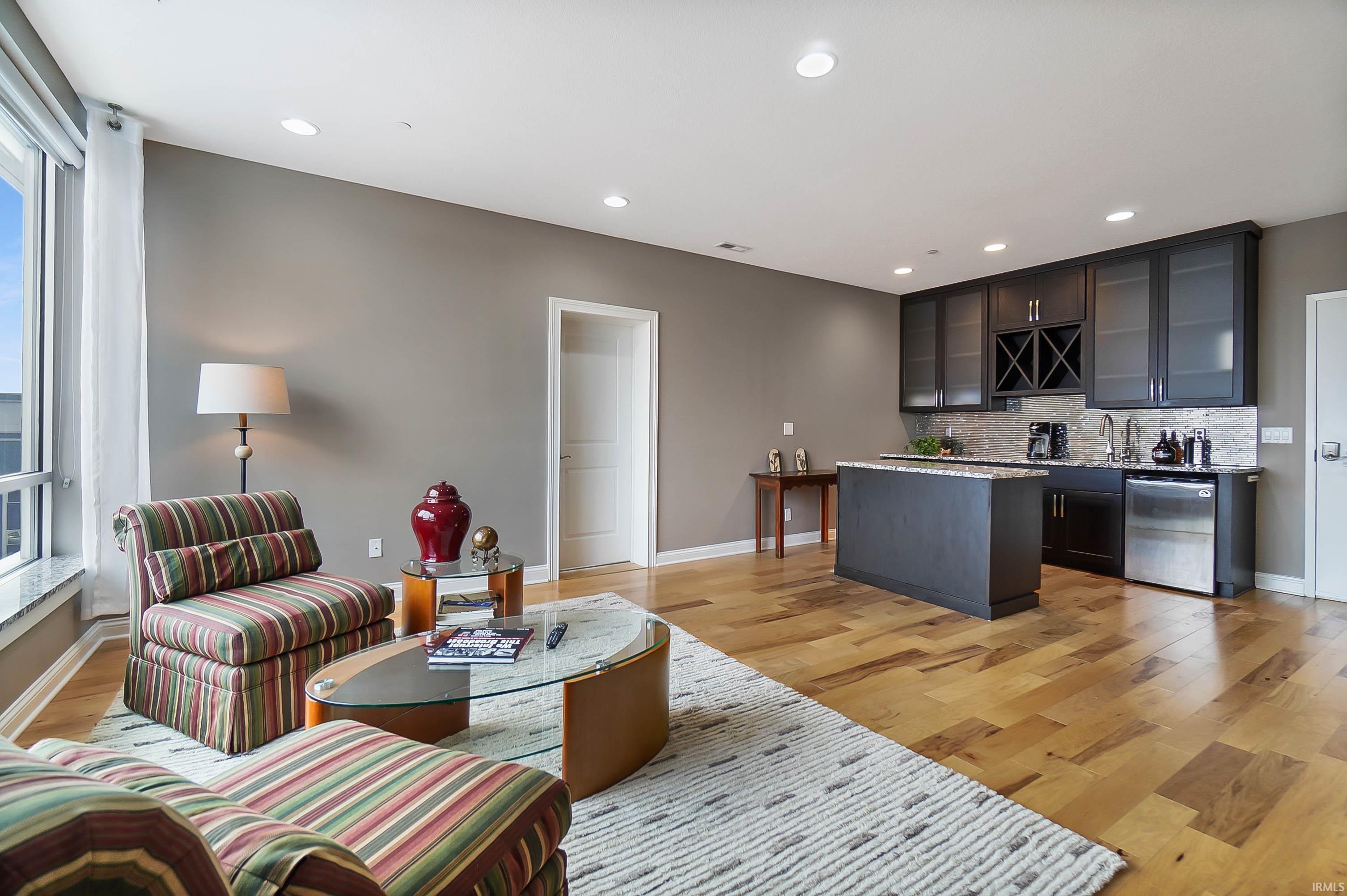 Living area featuring bar with sink, light wood-style flooring, and recessed lighting