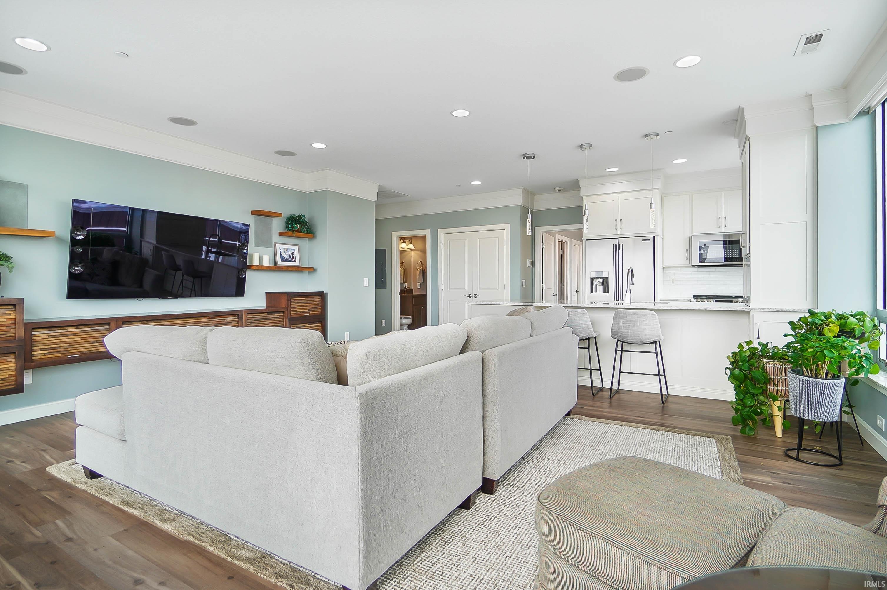 Living room with dark wood-type flooring, ornamental molding, and recessed lighting