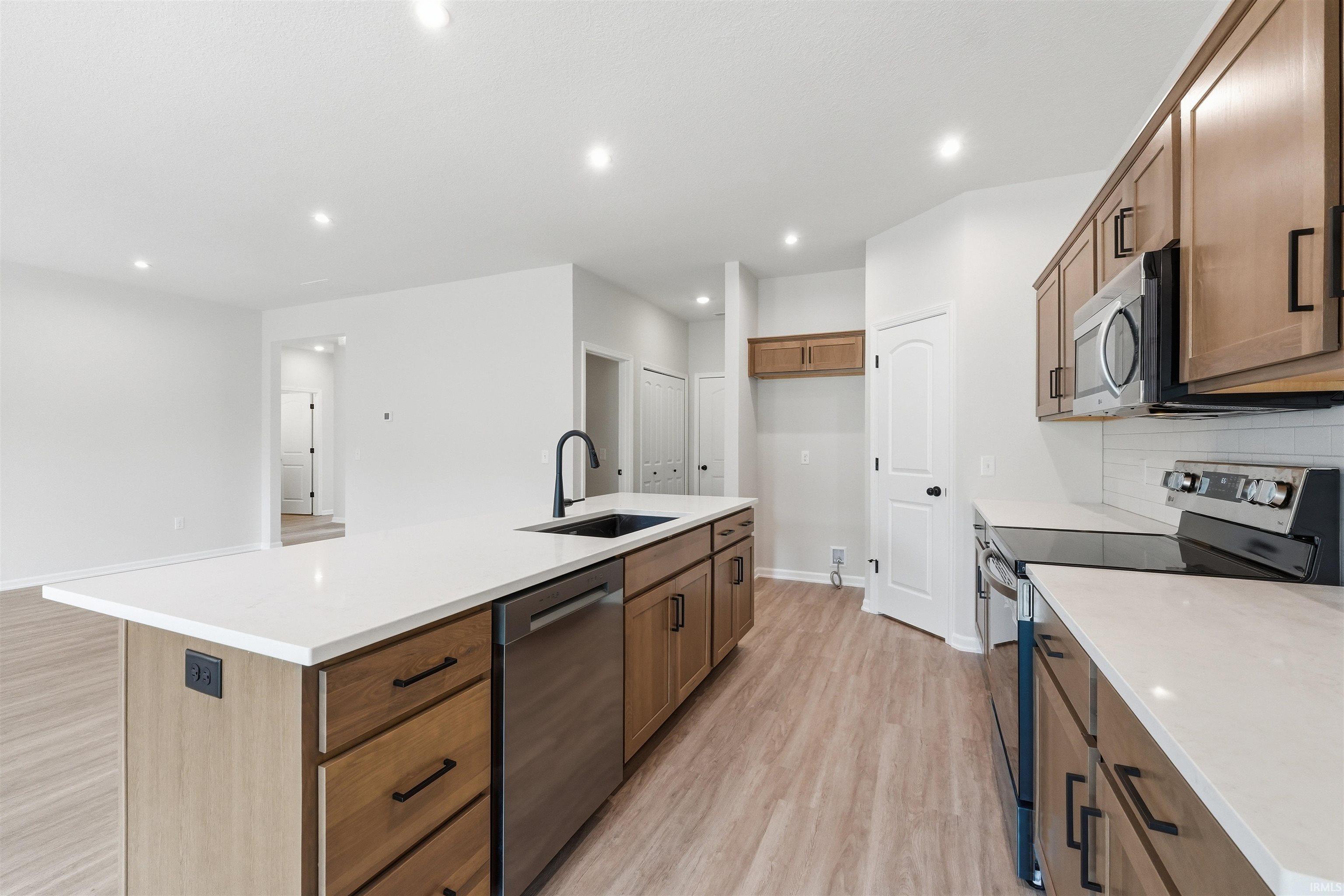 Kitchen featuring a central island with white countertop and black sink, wood-finish cabinetry, stainless steel appliances, and recessed lighting
