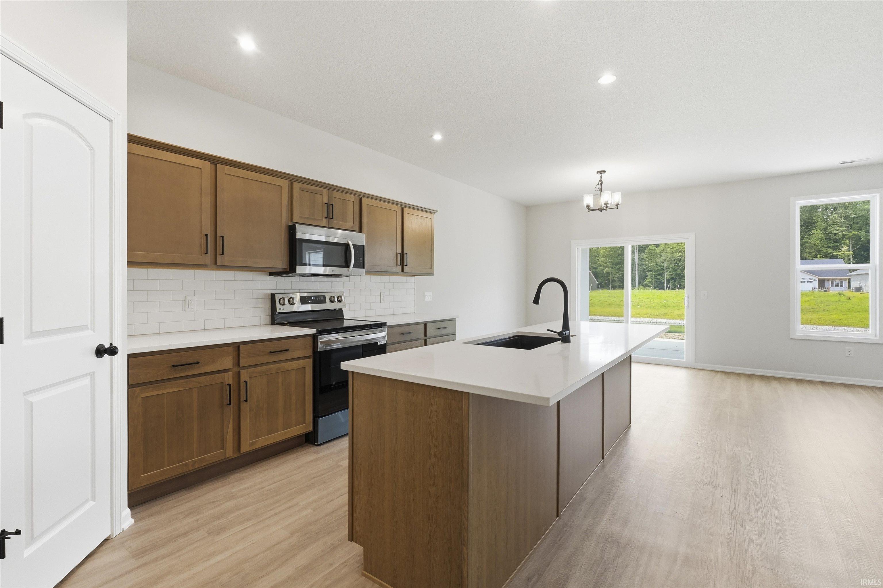 Modern kitchen featuring wood-finish cabinetry, white subway tile backsplash, and stainless steel appliances