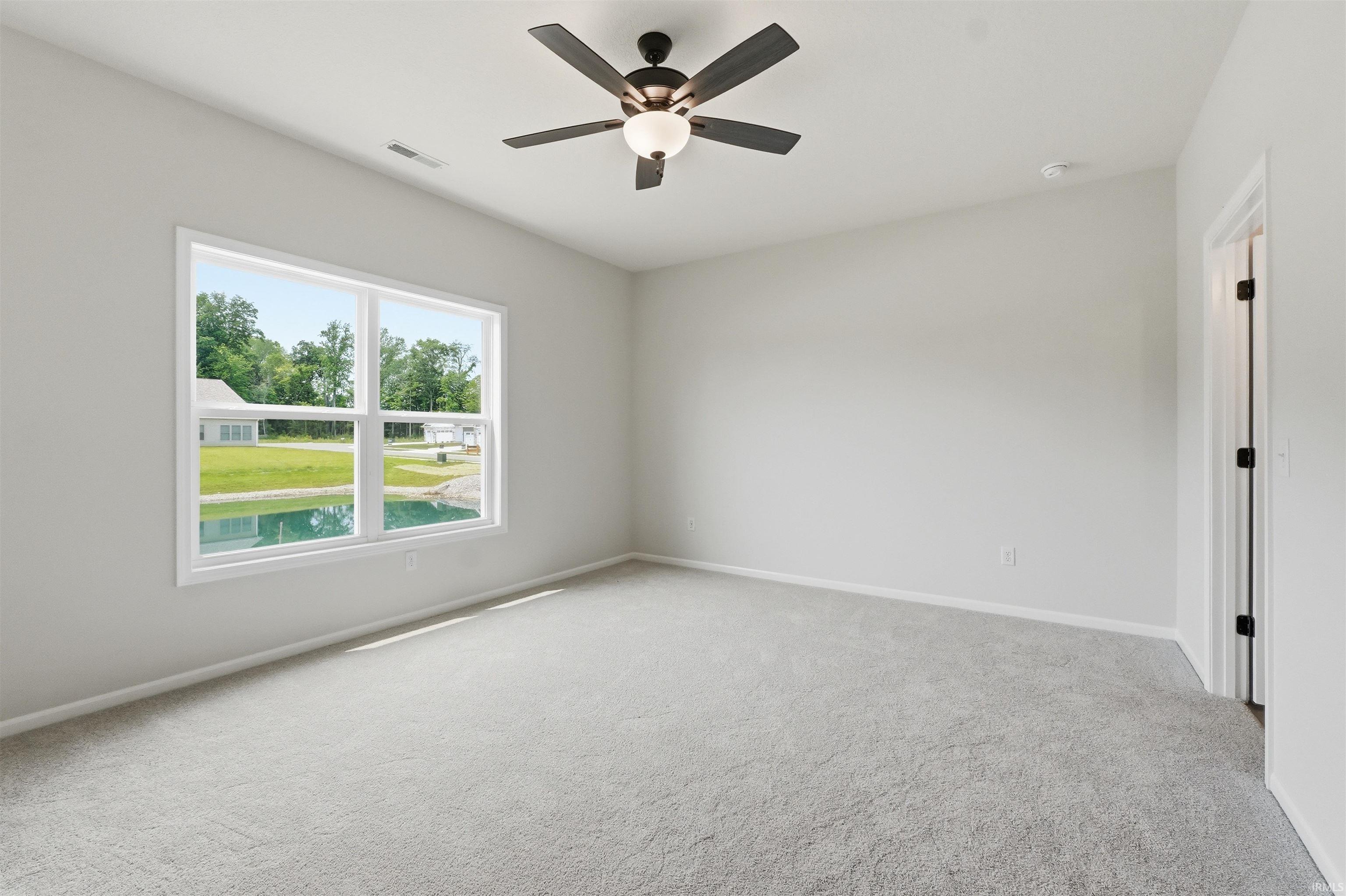 Bright Owner Suite Bedroom featuring a large window, plush carpet flooring, a ceiling fan with integrated lighting, and a white interior door with dark hardware