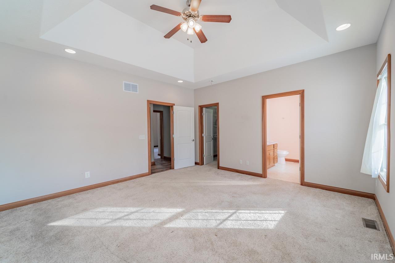 Unfurnished bedroom with light carpet, recessed lighting, ensuite bath, ceiling fan, and a tray ceiling