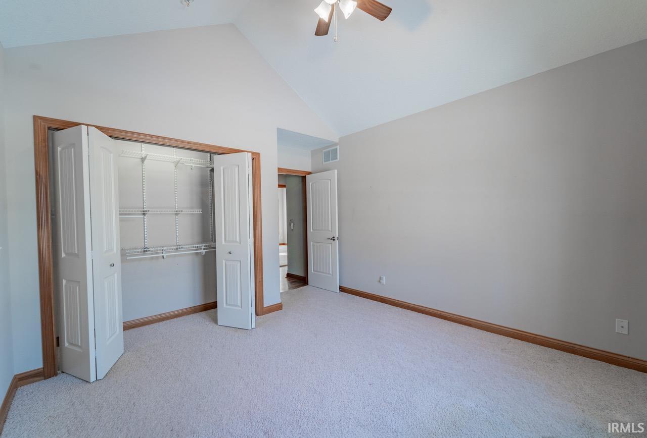 Unfurnished bedroom with light colored carpet, a closet, a ceiling fan, and a high ceiling
