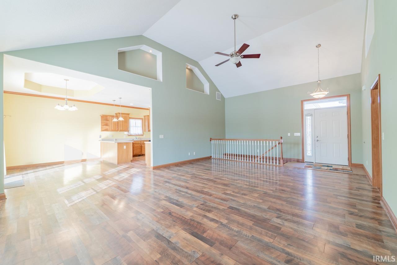 Unfurnished living room featuring a ceiling fan, a high ceiling, wood finished floors, a chandelier, and crown molding