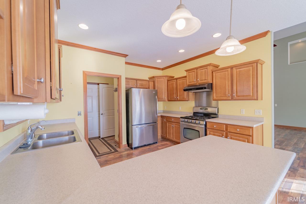 Kitchen with stainless steel appliances, light countertops, dark wood-style floors, a peninsula, and crown molding