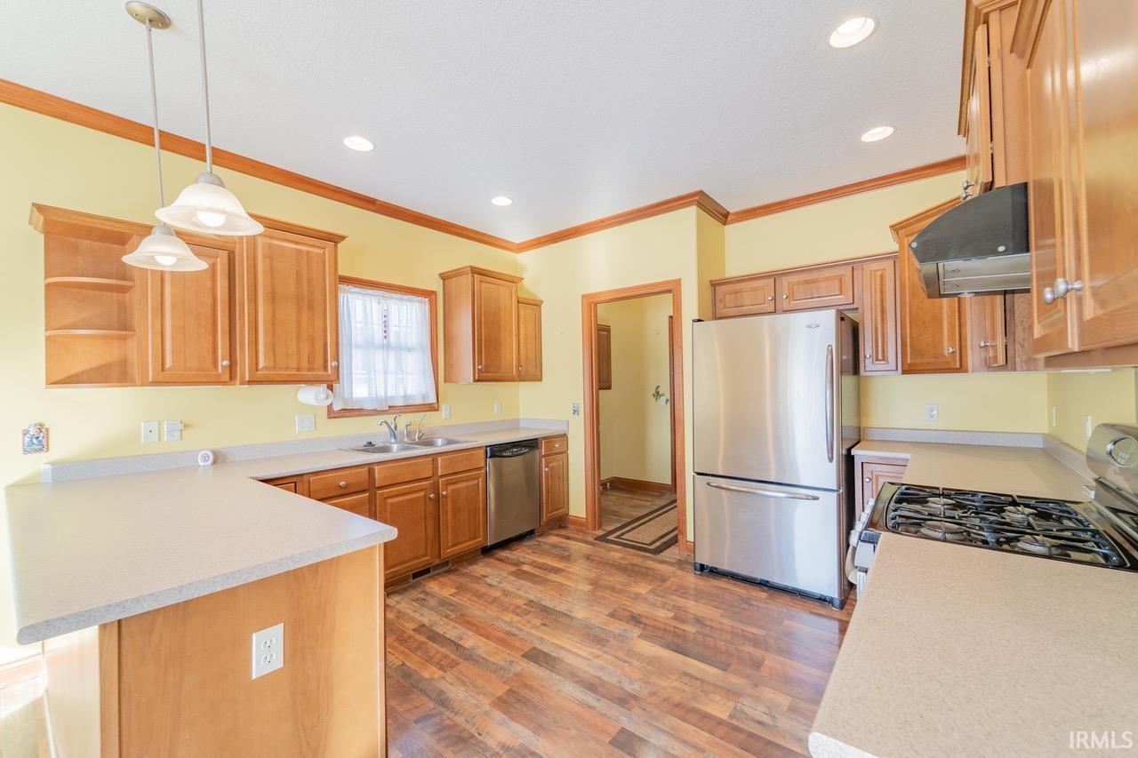 Kitchen featuring stainless steel appliances, a peninsula, light countertops, hanging light fixtures, and range hood