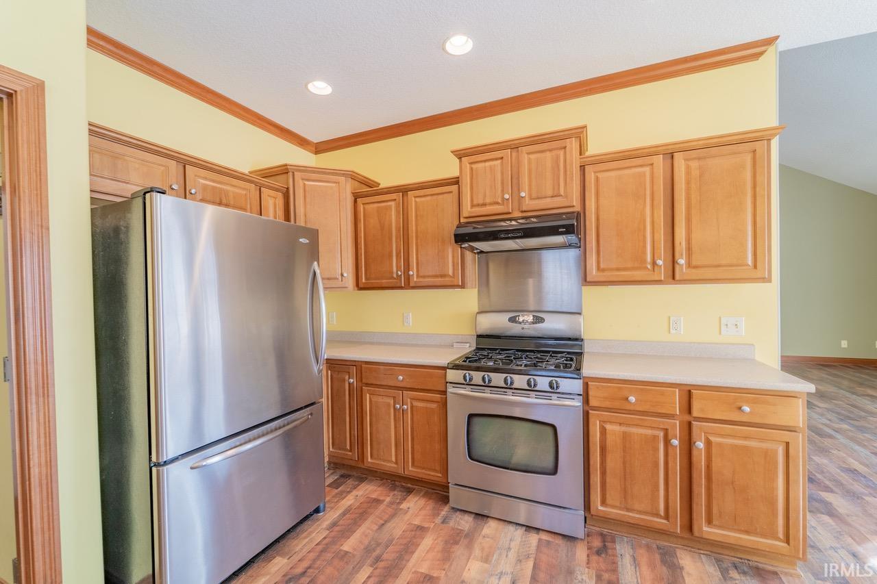 Kitchen with stainless steel appliances, light wood-type flooring, ornamental molding, light countertops, and wood finish cabinetry