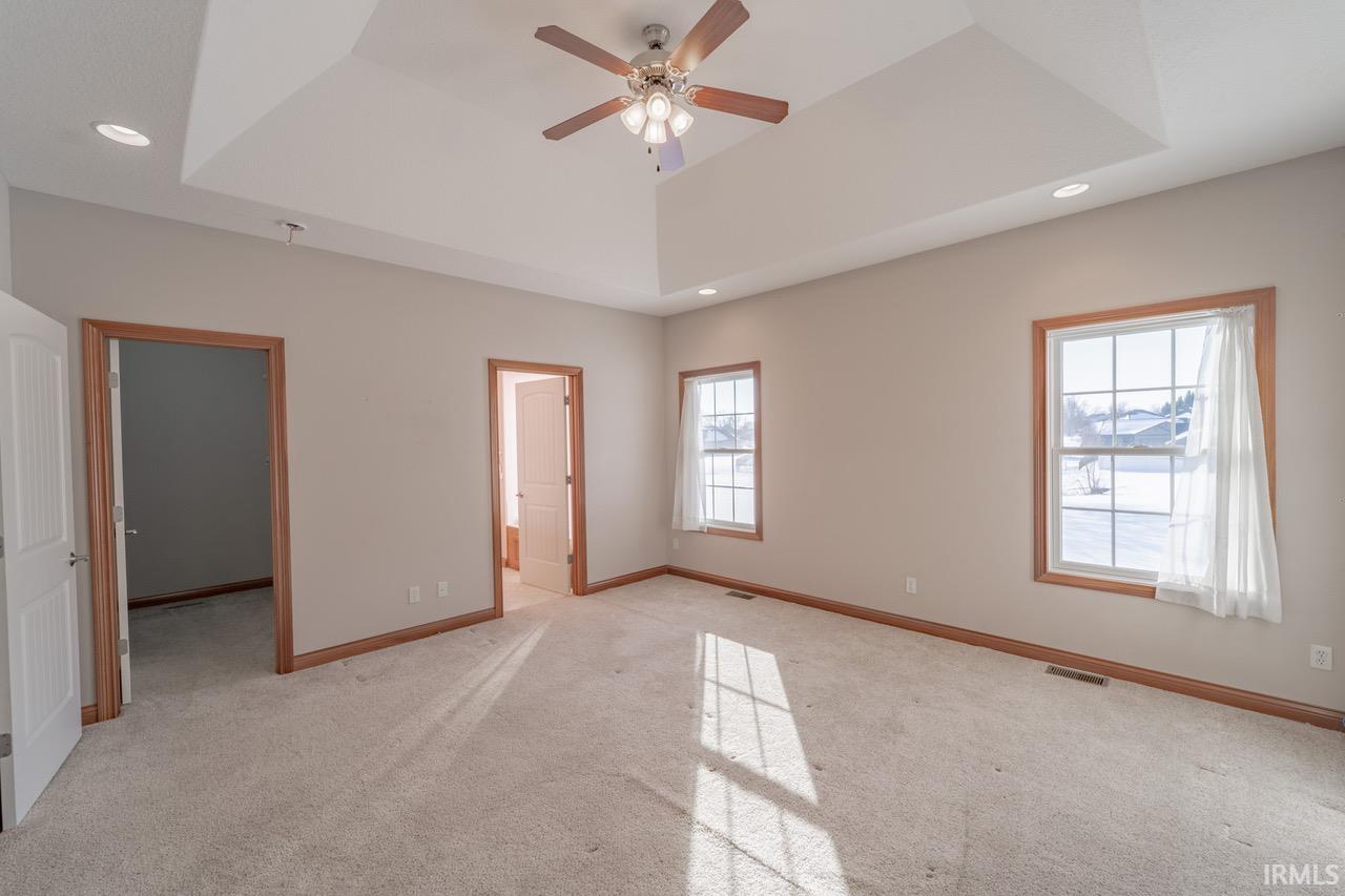 Unfurnished bedroom featuring recessed lighting, light colored carpet, a ceiling fan, a raised ceiling, and ensuite bath