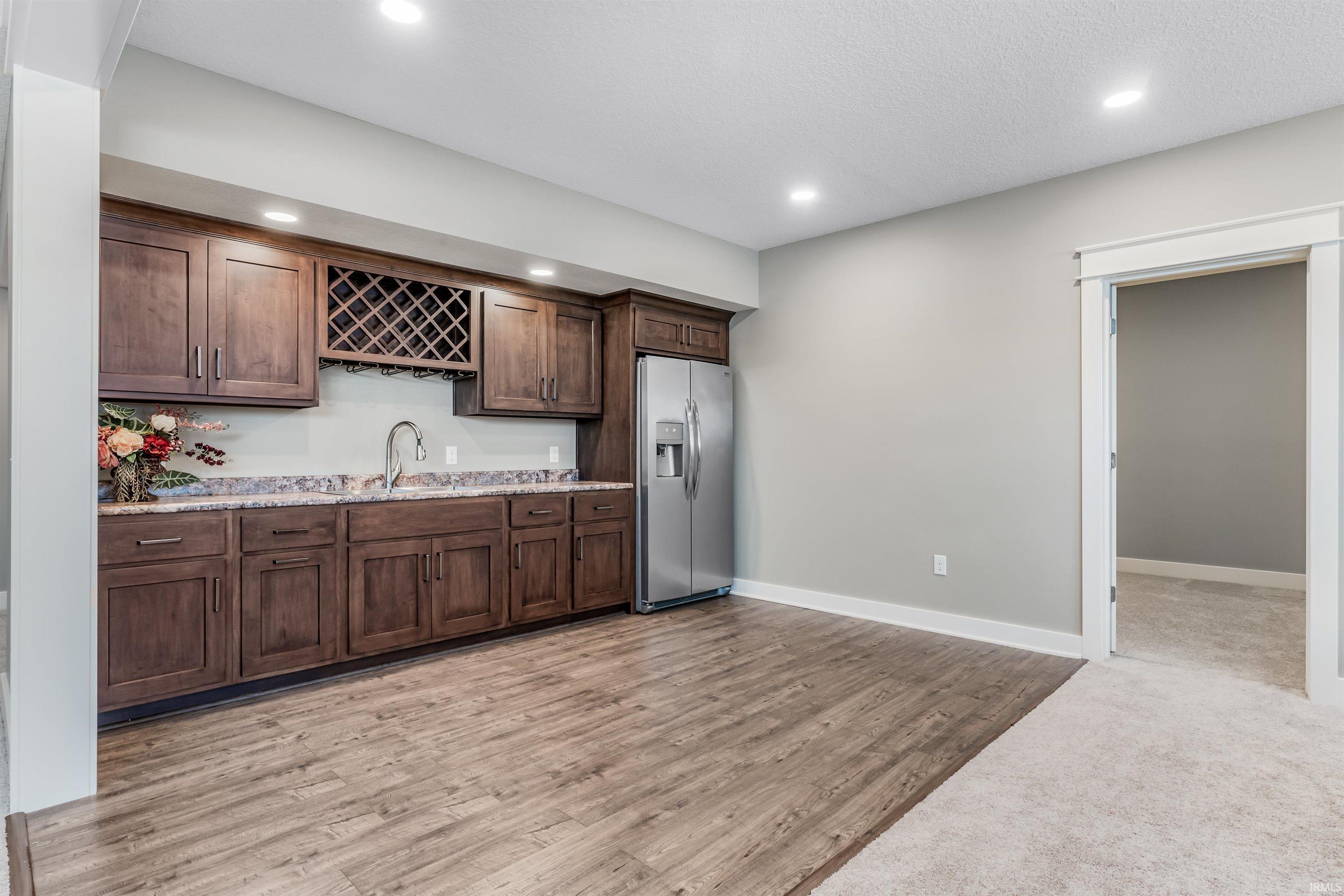 Kitchen featuring dark wood finish cabinetry, stainless steel refrigerator with ice dispenser, light wood-style floors, recessed lighting, and light stone counters