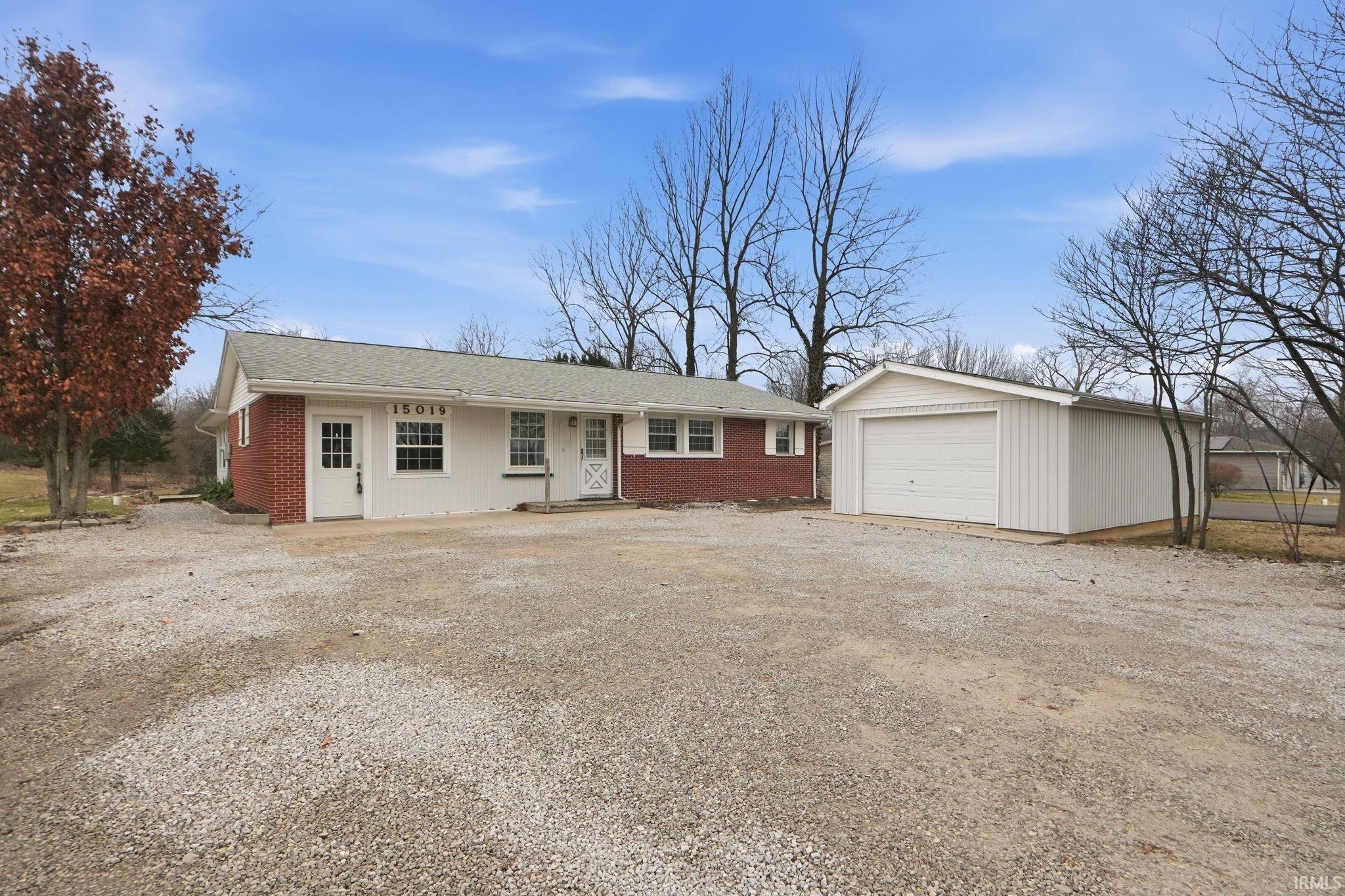 Ranch-style home featuring driveway, an outbuilding, a detached garage, and brick siding