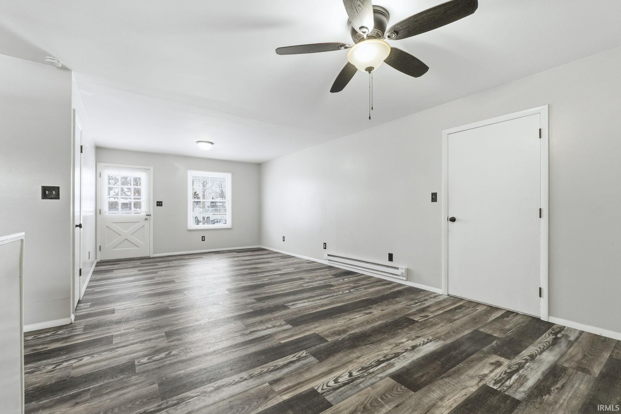 Unfurnished living room with baseboard heating, ceiling fan, and dark wood-type flooring