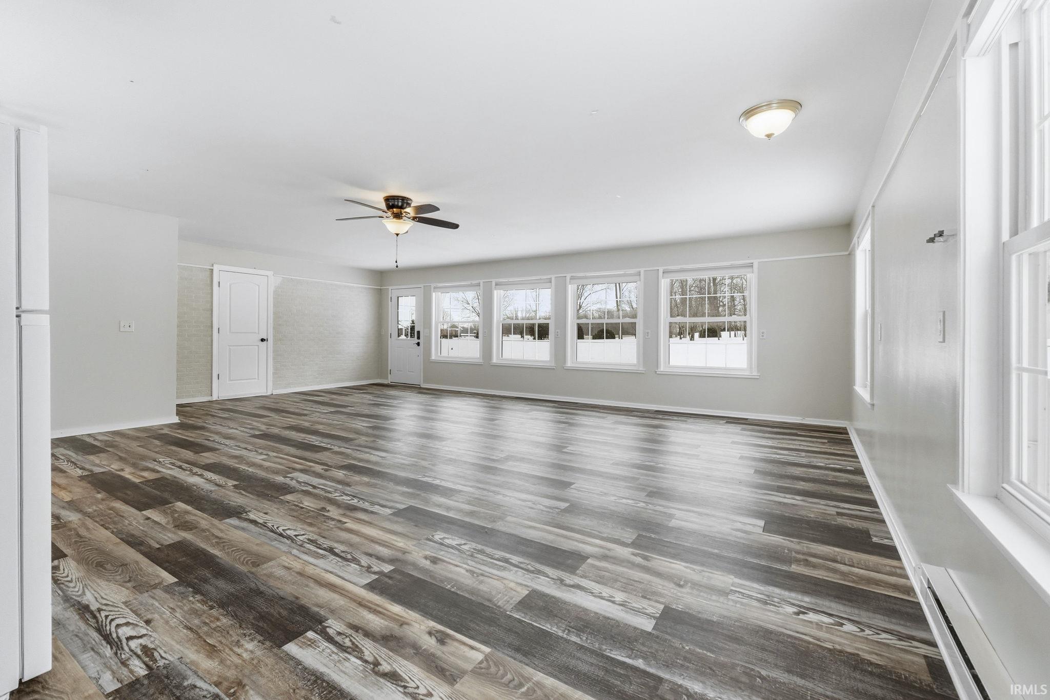 Unfurnished living room featuring a baseboard heating unit, a ceiling fan, and dark wood finished floors