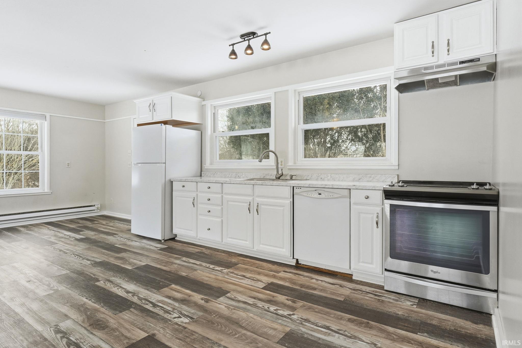 Kitchen featuring white cabinetry, white appliances, light countertops, and dark wood-type flooring