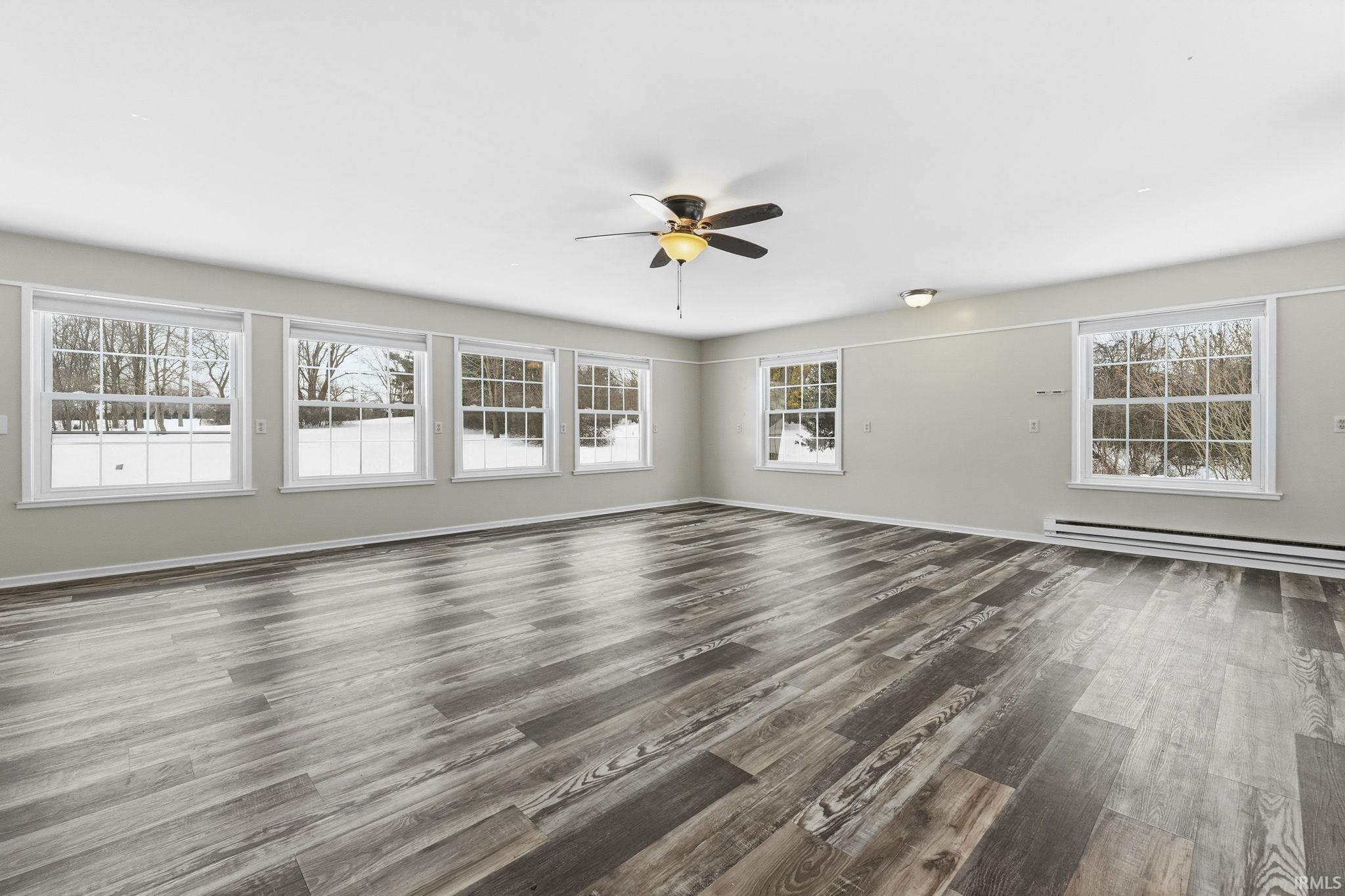 Unfurnished room with ceiling fan, a baseboard heating unit, and dark wood finished floors