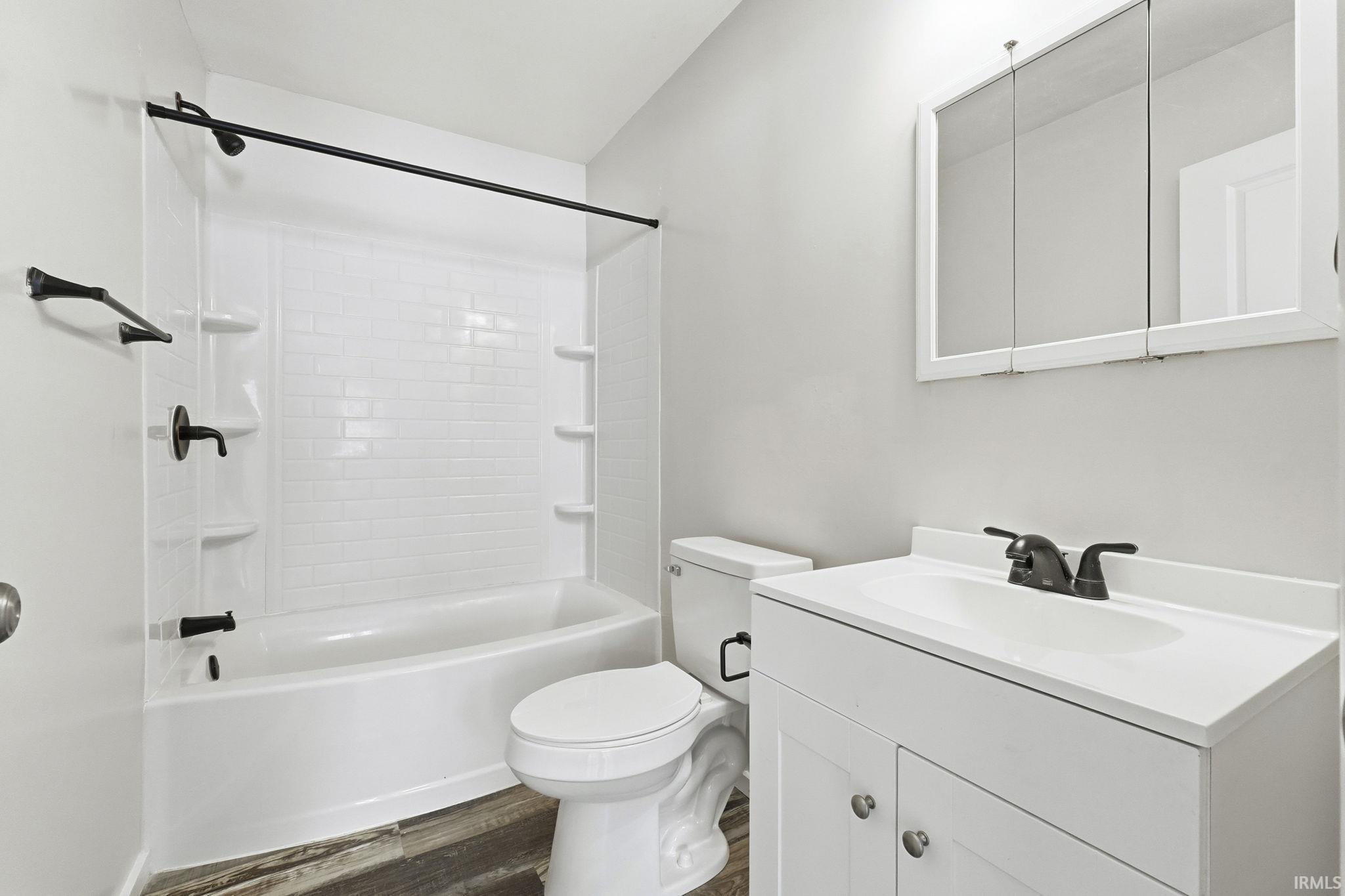 Bathroom featuring vanity, shower / tub combination, and dark wood-type flooring