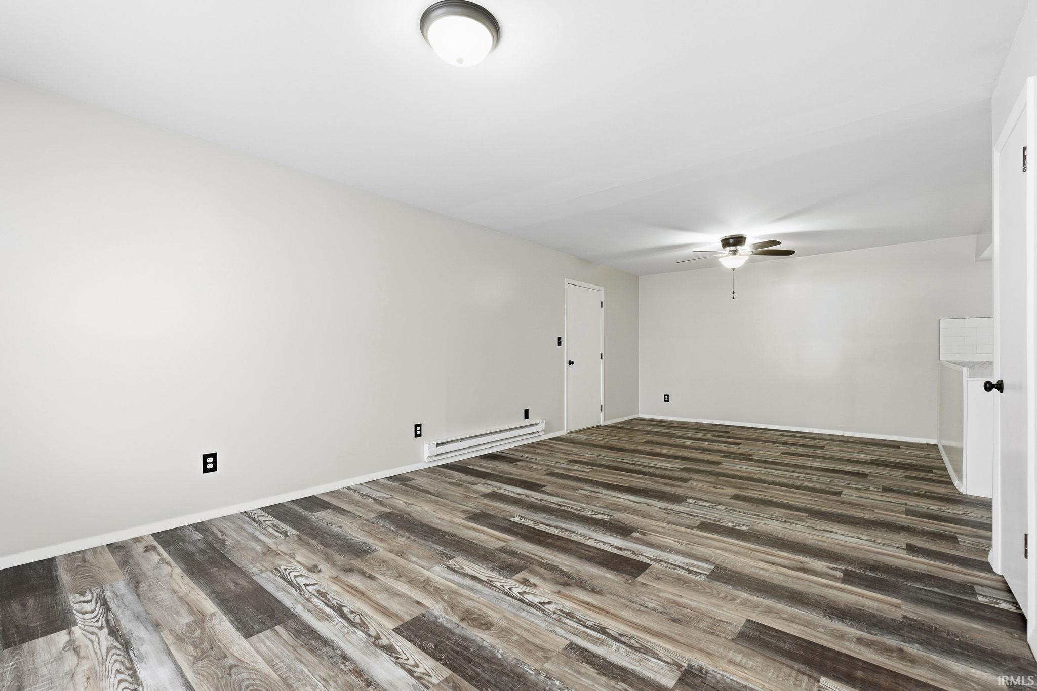Empty room featuring a baseboard radiator, dark wood finished floors, and a ceiling fan