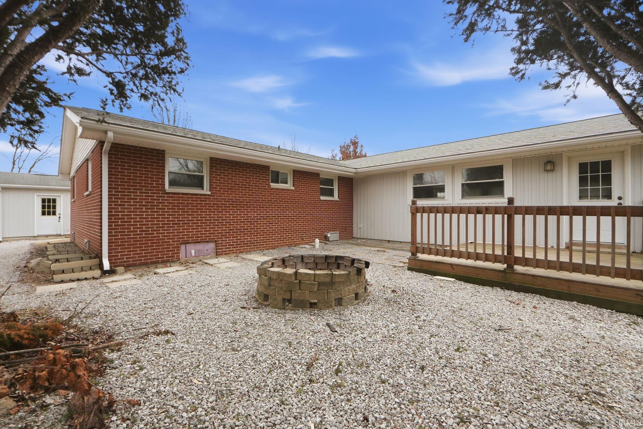 Back of property with brick siding, a fire pit, a deck, crawl space, and roof with shingles