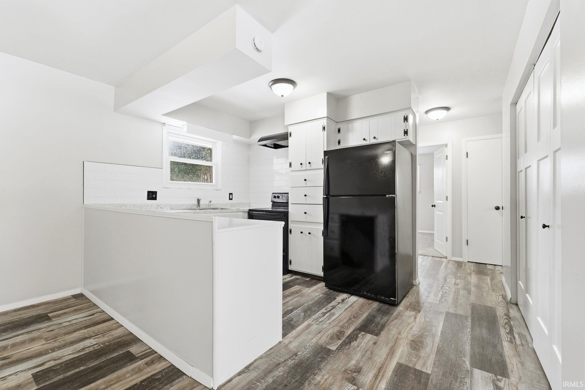 Kitchen with white cabinetry, black appliances, light countertops, light wood-style flooring, and a peninsula