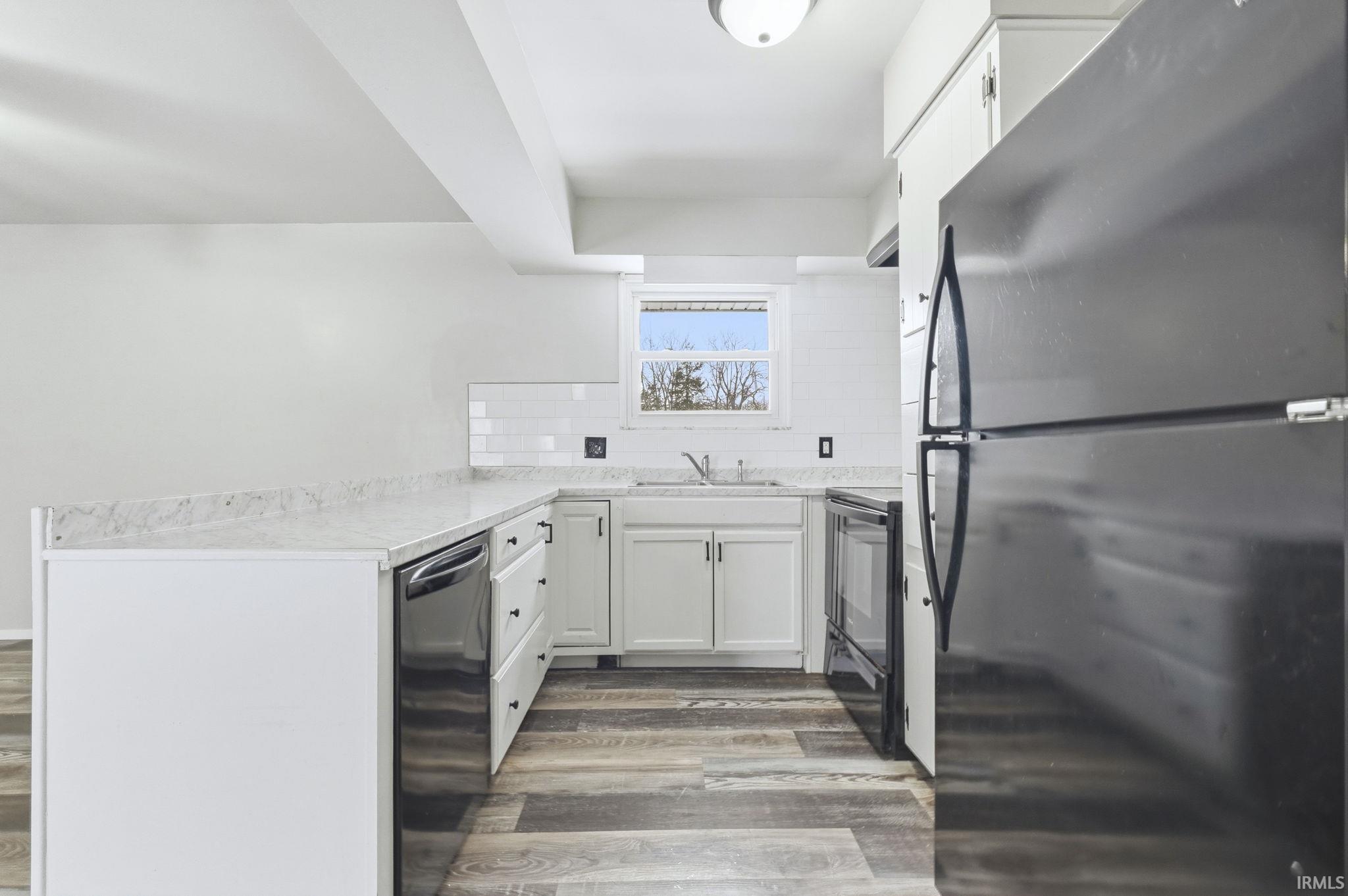 Kitchen with black appliances, white cabinets, light countertops, dark wood finished floors, and a peninsula