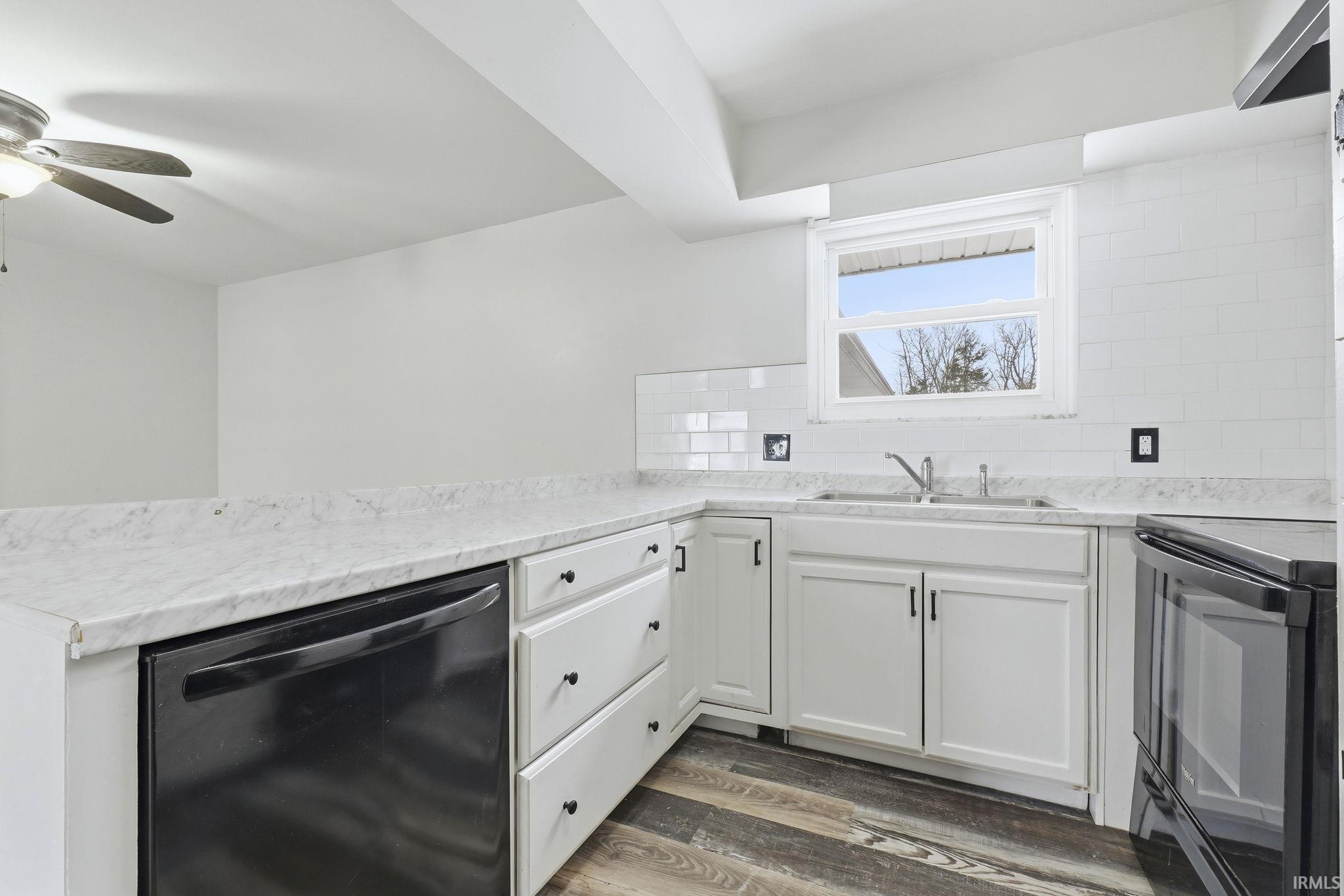 Kitchen featuring black appliances, white cabinetry, backsplash, dark wood-type flooring, and a peninsula