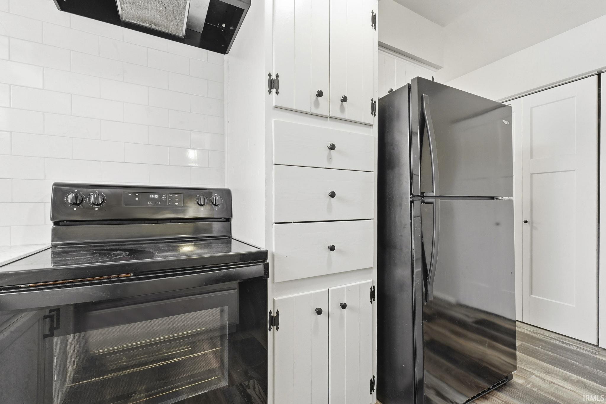 Kitchen with black appliances, range hood, white cabinets, and light wood finished floors