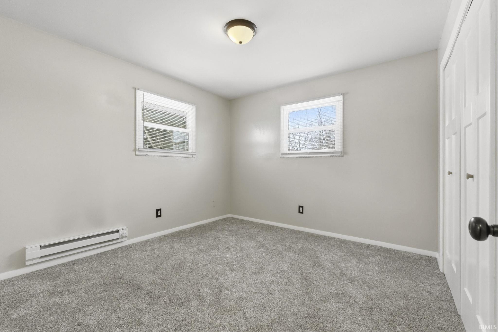 Unfurnished bedroom with a baseboard heating unit, carpet flooring, multiple windows, and a closet