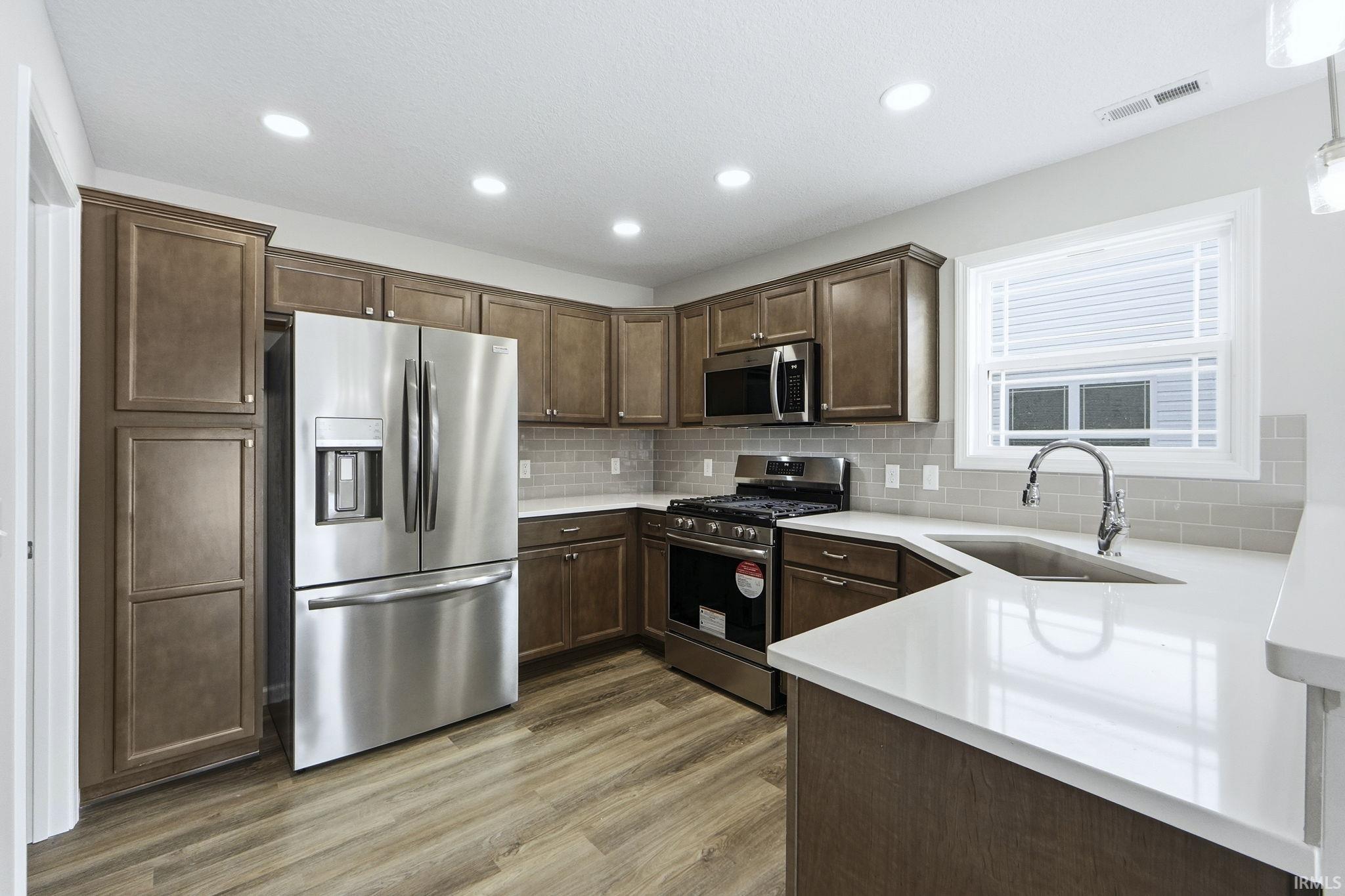 Kitchen with stainless steel appliances, dark wood finish cabinetry, dark wood finished floors, decorative backsplash, and light stone countertops