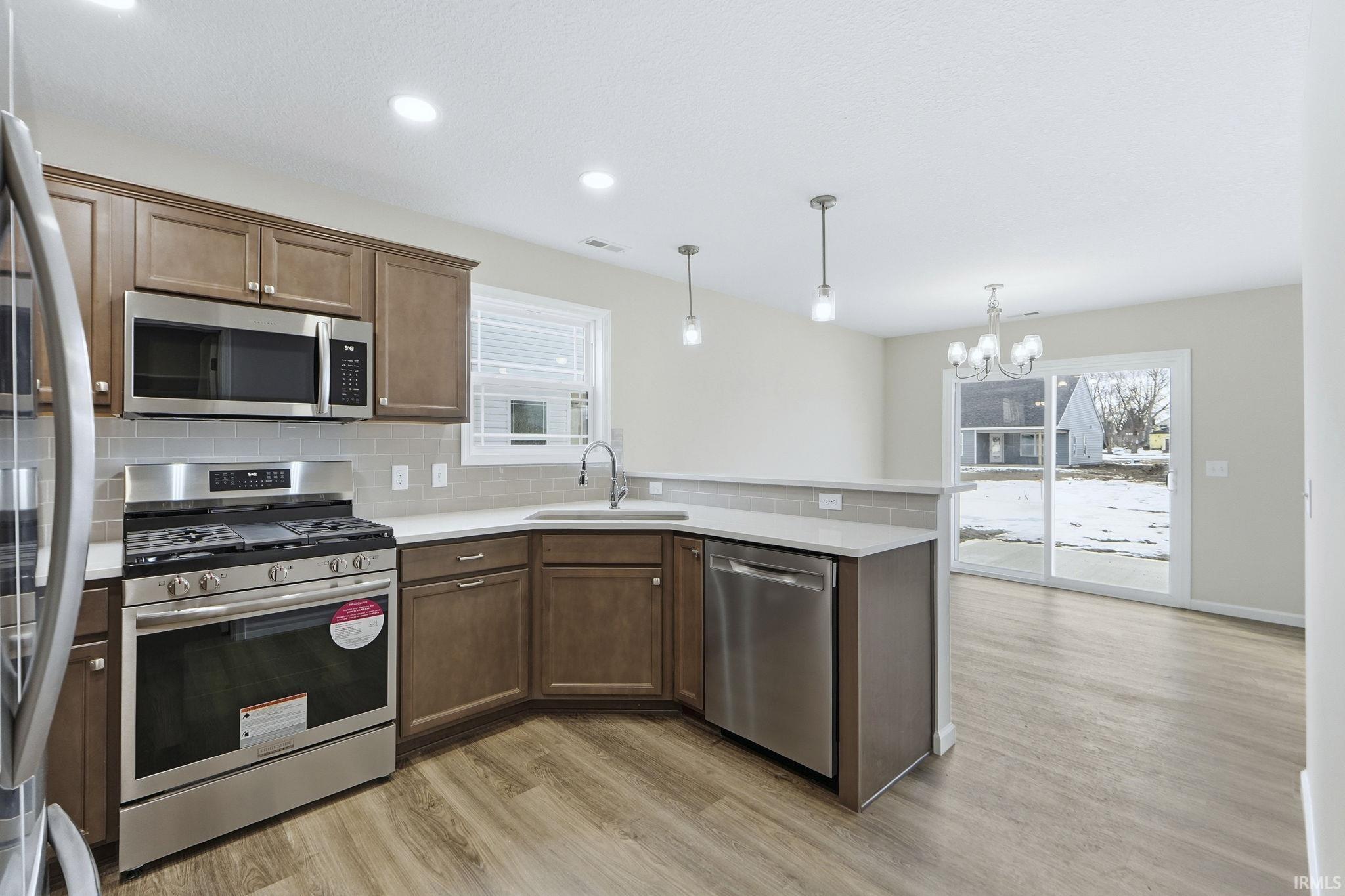 Kitchen with stainless steel appliances, a peninsula, tasteful backsplash, and light wood finished floors
