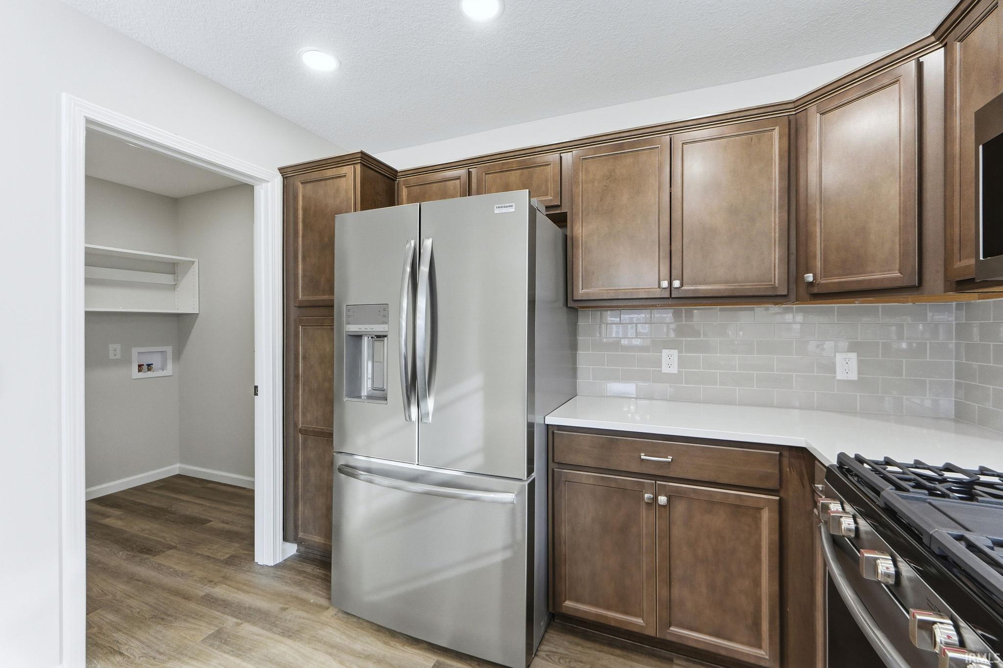 Kitchen featuring stainless steel appliances, light wood-style flooring, decorative backsplash, and light stone counters