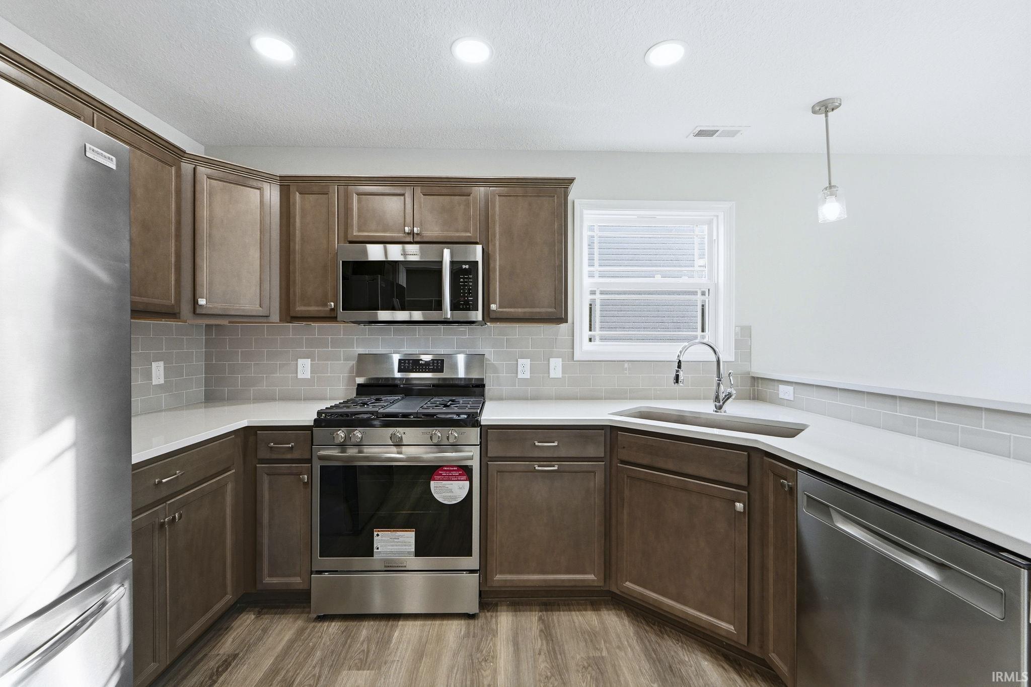 Kitchen featuring stainless steel appliances, light wood-style floors, dark wood finish cabinetry, and pendant lighting