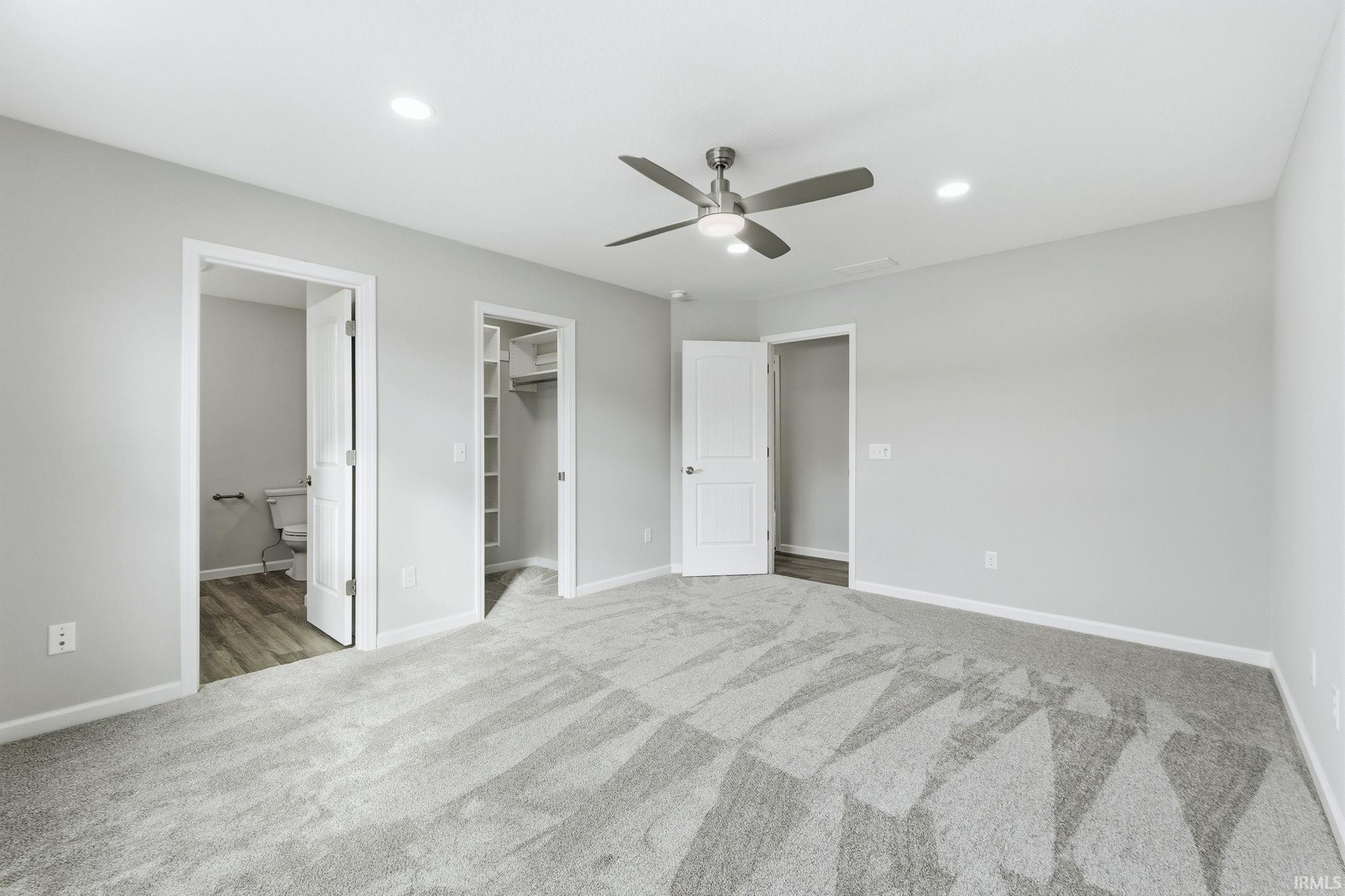 Unfurnished bedroom with ensuite bath, a spacious closet, a ceiling fan, light carpet, and recessed lighting