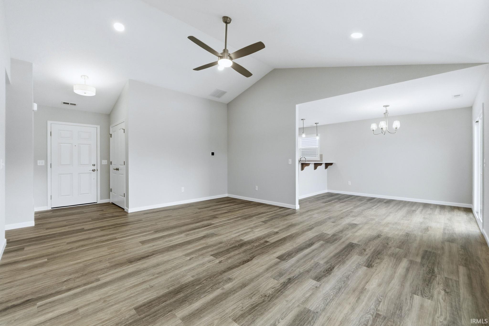 Unfurnished living room with a ceiling fan, light wood-style flooring, lofted ceiling, and a chandelier