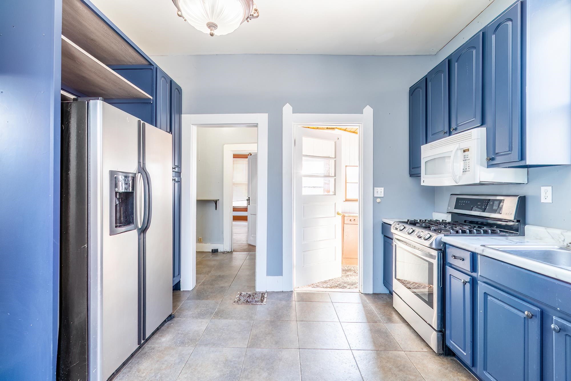 Kitchen featuring blue cabinetry, stainless steel appliances, light countertops, tile flooring and open shelves