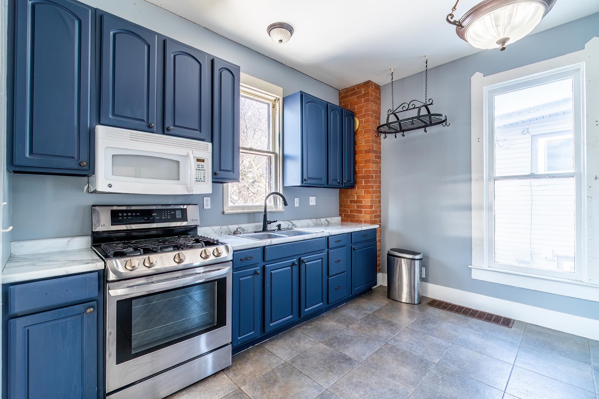 Kitchen with blue cabinets, stainless steel range with gas cooktop, white microwave, tile flooring and light countertops
