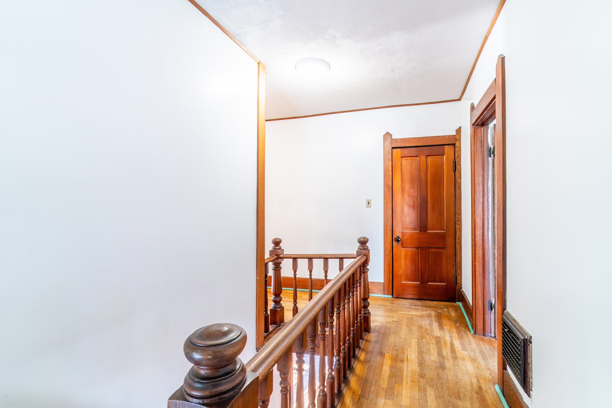 Hallway with an upstairs landing, hardwood flooring, and ornamental molding.