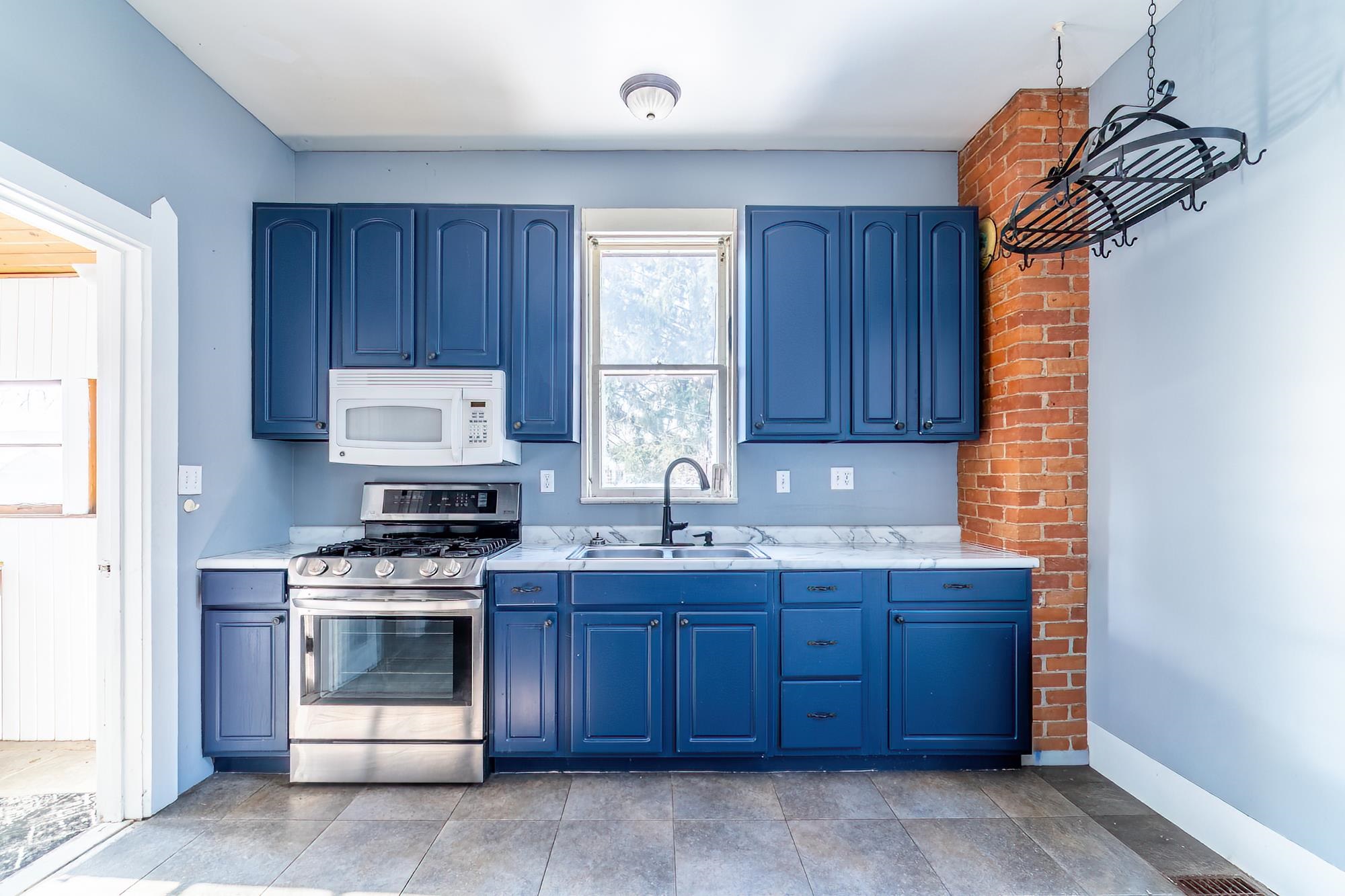 Kitchen with blue cabinets, gas range, white microwave, tile flooring, and light countertops