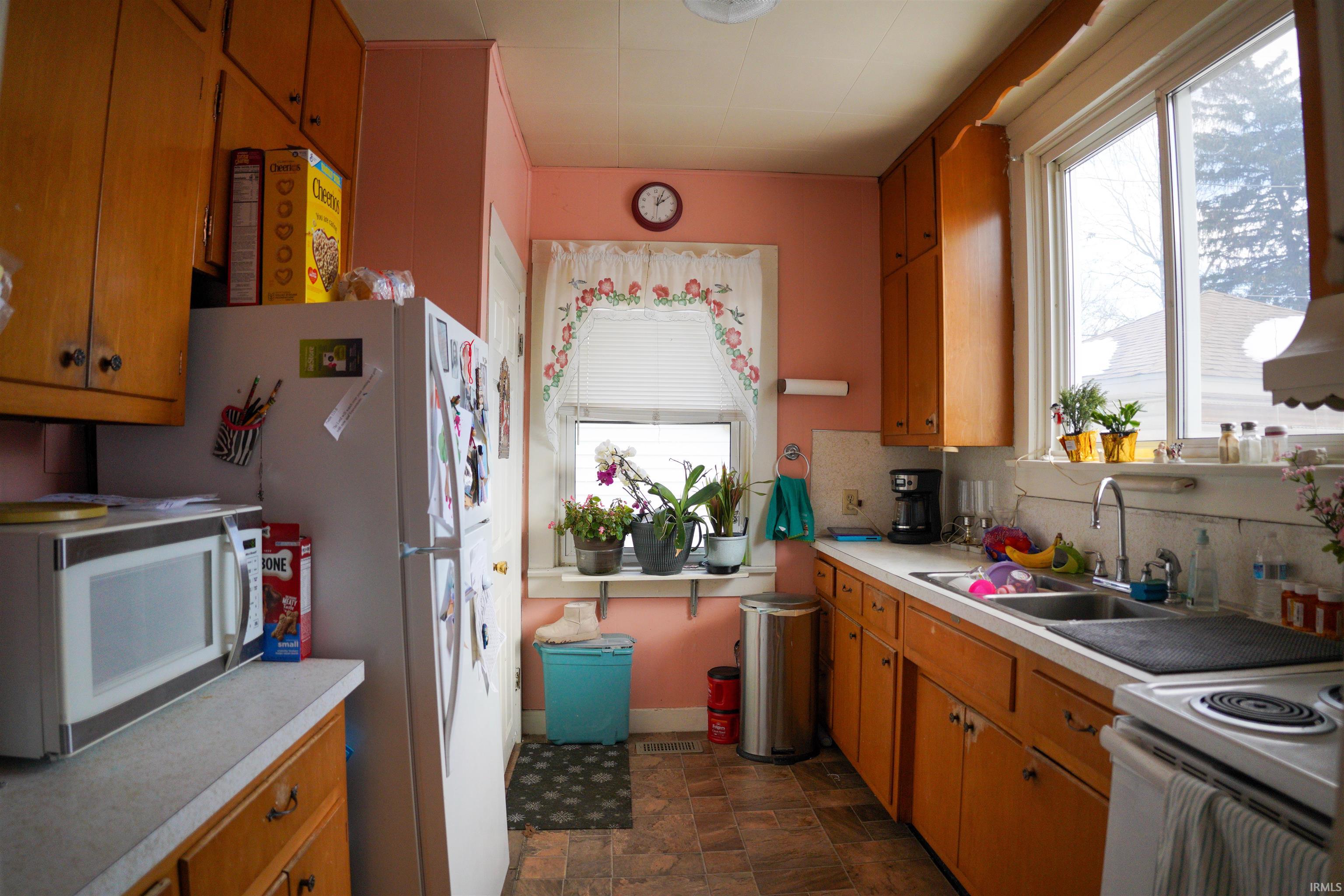 Kitchen featuring wood finish cabinetry, white appliances, stone finish floors, light countertops, and backsplash