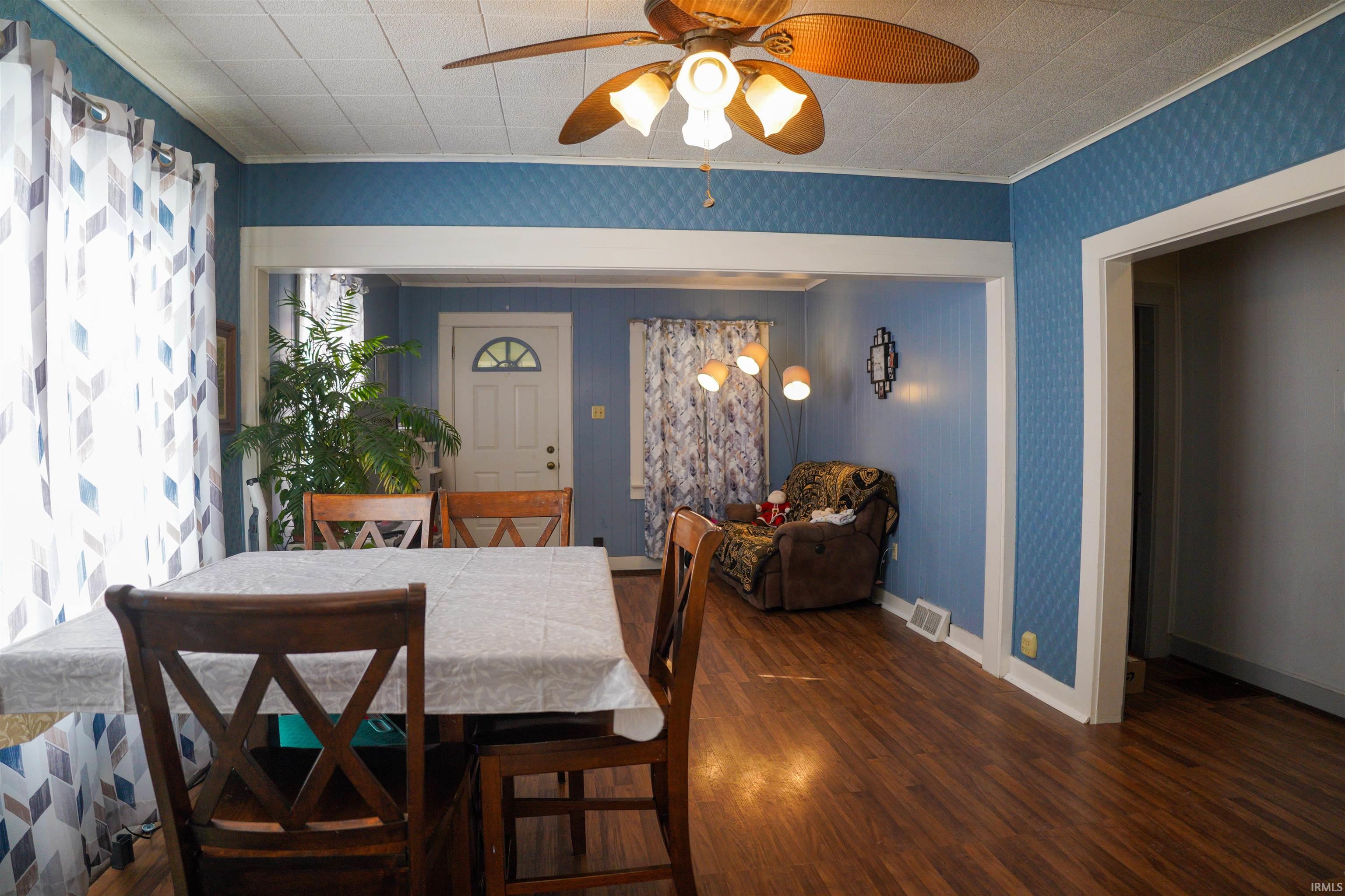 Dining area featuring dark wood-style floors, a ceiling fan, ornamental molding, and wallpapered walls