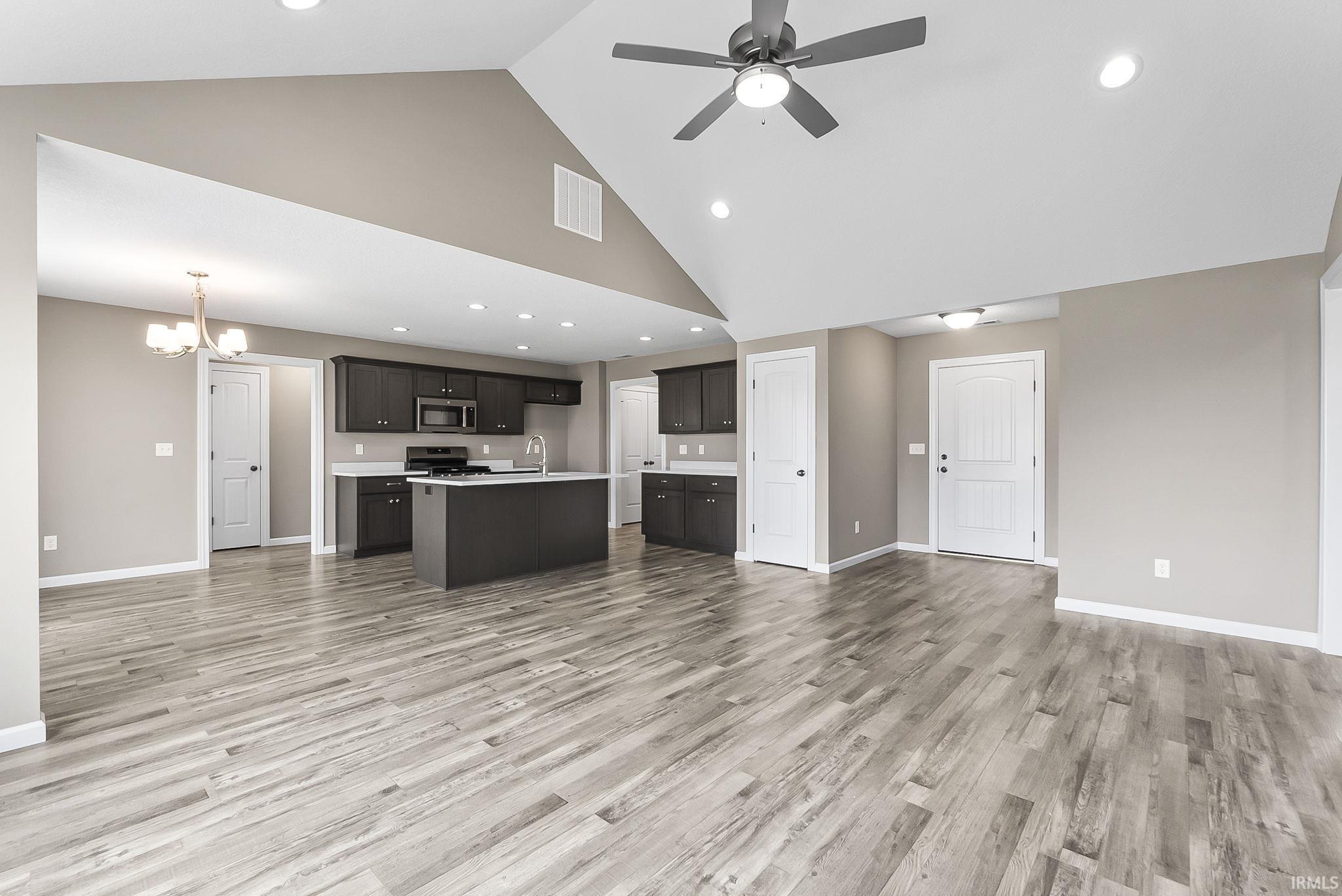 Unfurnished living room featuring a chandelier, ceiling fan, light wood-style floors, and vaulted ceiling