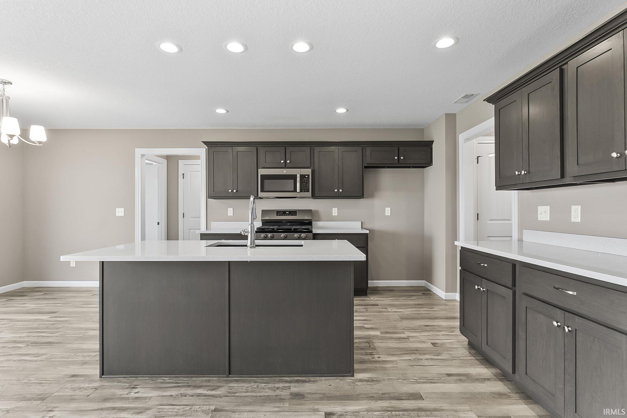 Kitchen featuring light wood-style floors, a kitchen island with sink, stainless steel appliances, light stone counters, and dark wood finish cabinets