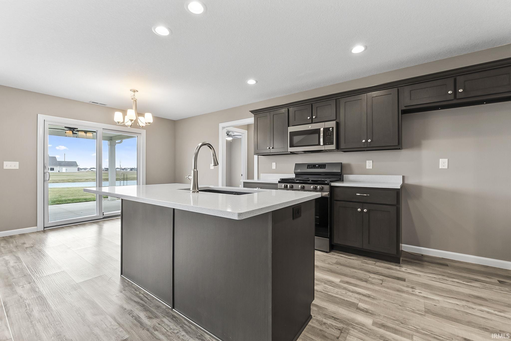 Kitchen featuring stainless steel appliances, a chandelier, light wood-style floors, an island with sink, and light stone counters