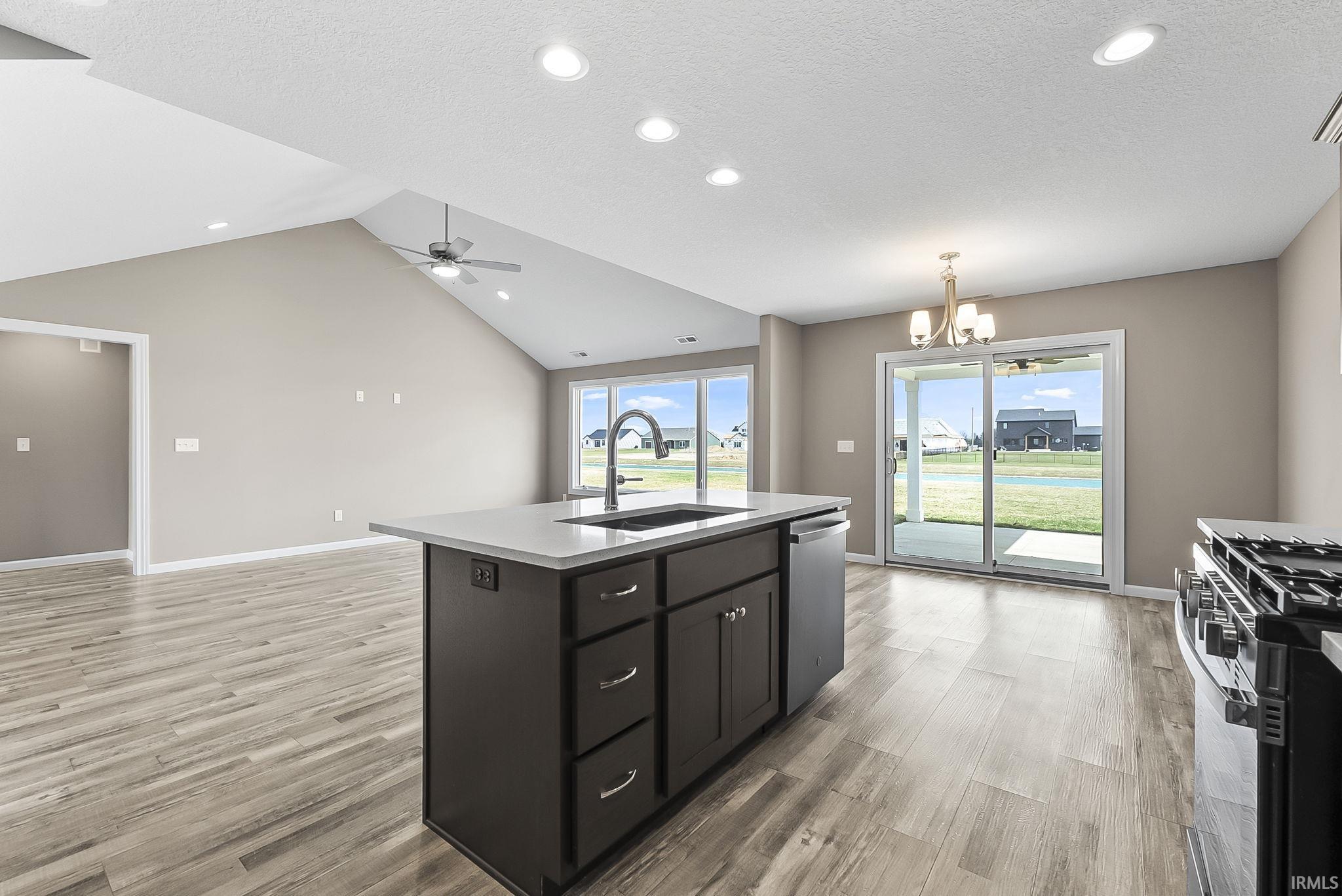Kitchen featuring suspended lighting, a kitchen island with sink, open floor plan, light wood finished floors, and a textured ceiling